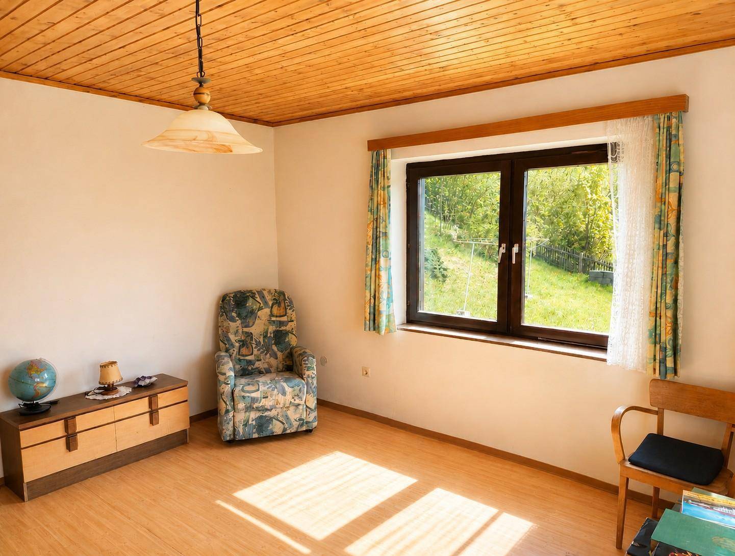 Helles Zimmer mit Holzdecke, Laminatboden und Blick auf die grüne Umgebung.