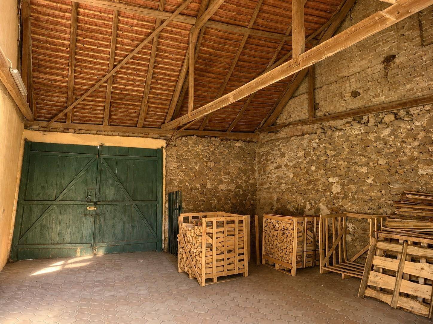 Rustikale Scheune mit freiliegenden Holzbalken, Steinmauern und großen grünen Holztoren.