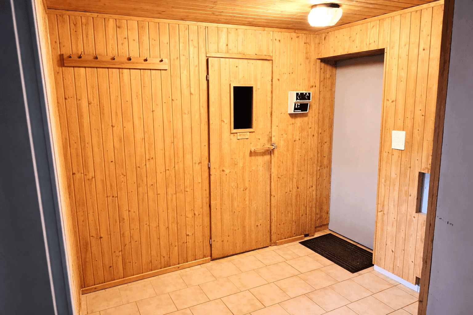 Holzverkleideter Vorraum mit Zugang zur Sauna und einem Schrank, gefliestem Boden.