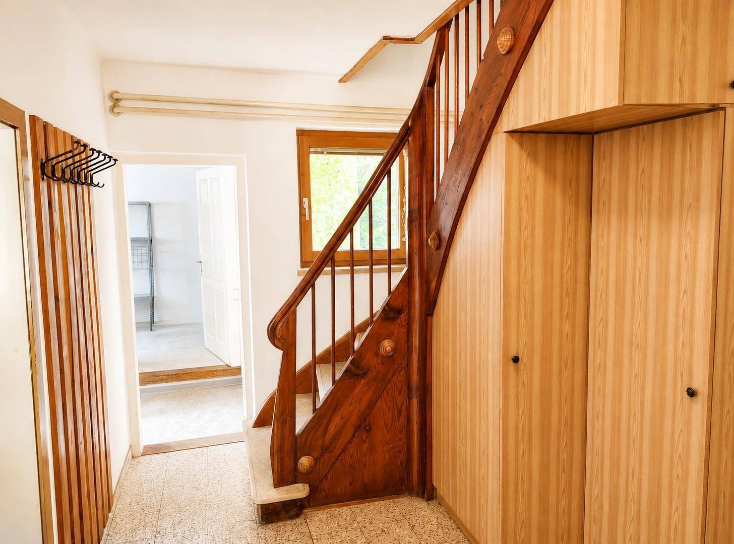 Flur mit Holztreppe, Einbauschränken und Terrazzoboden.