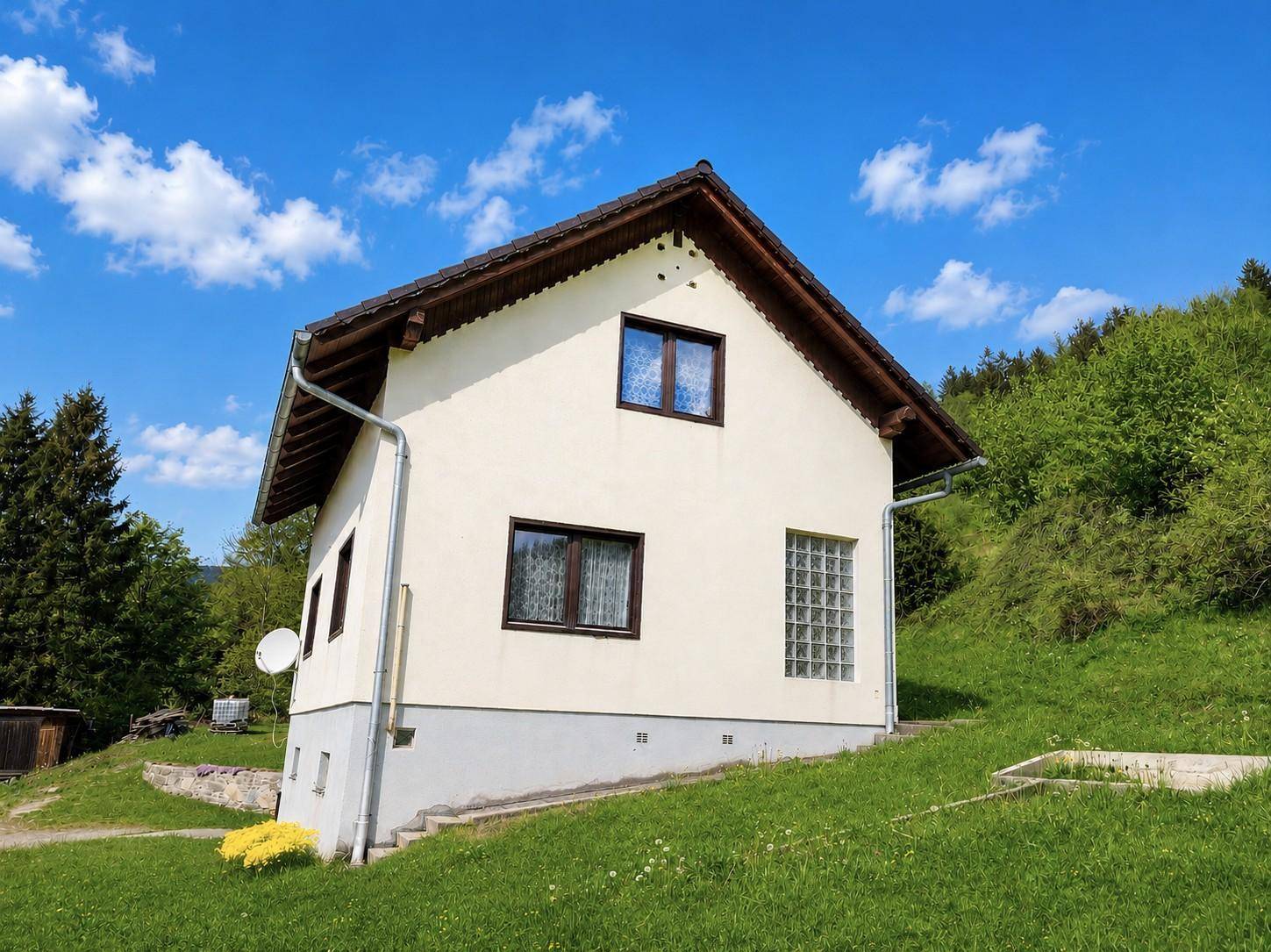 Weißes Einfamilienhaus mit Satteldach und Fenstern, umgeben von grüner Natur.