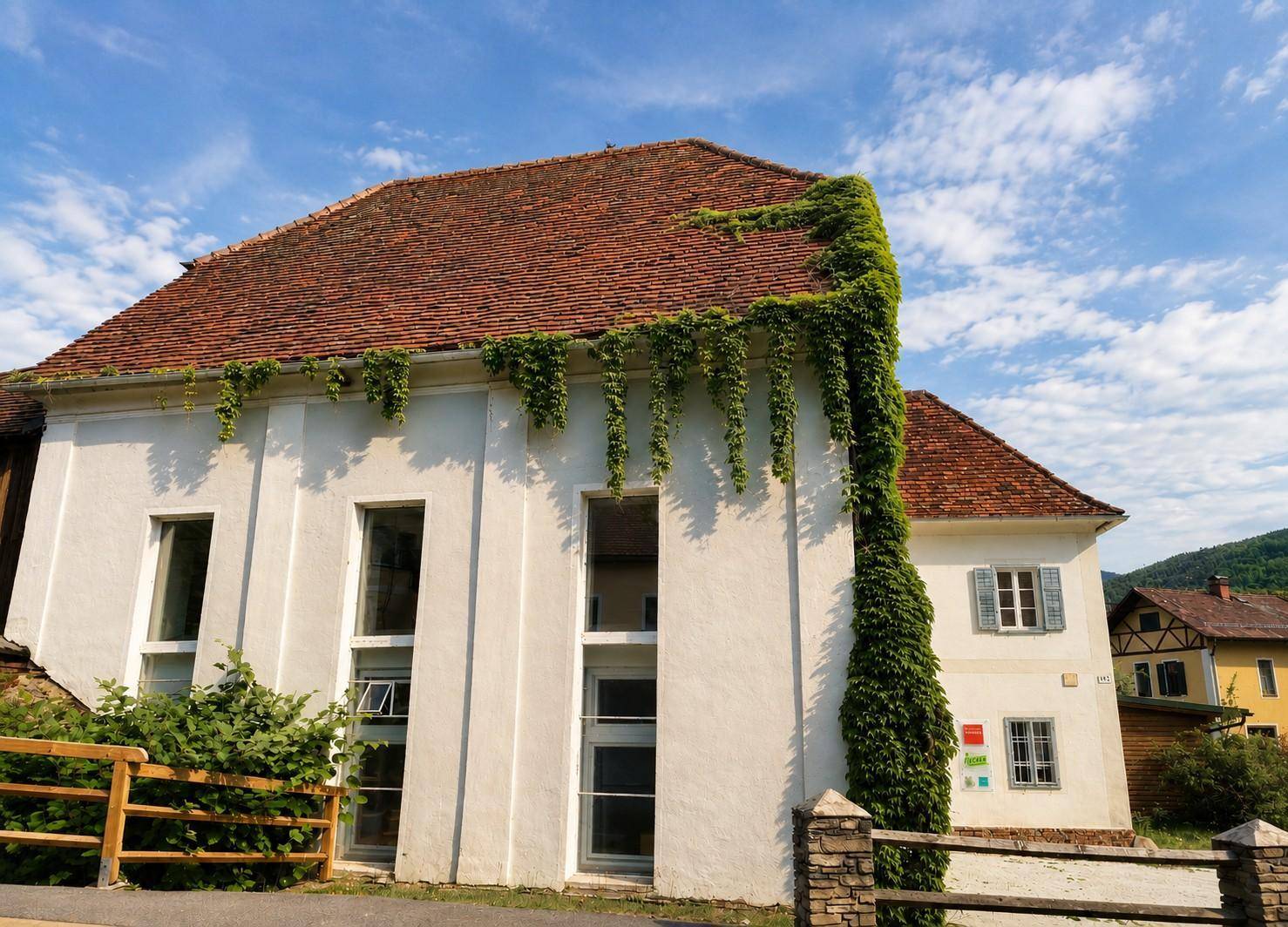 Fassade eines historischen Gebäudes mit hohen Fenstern und üppigem Efeu, das sich an der weißen Wand emporrankt.