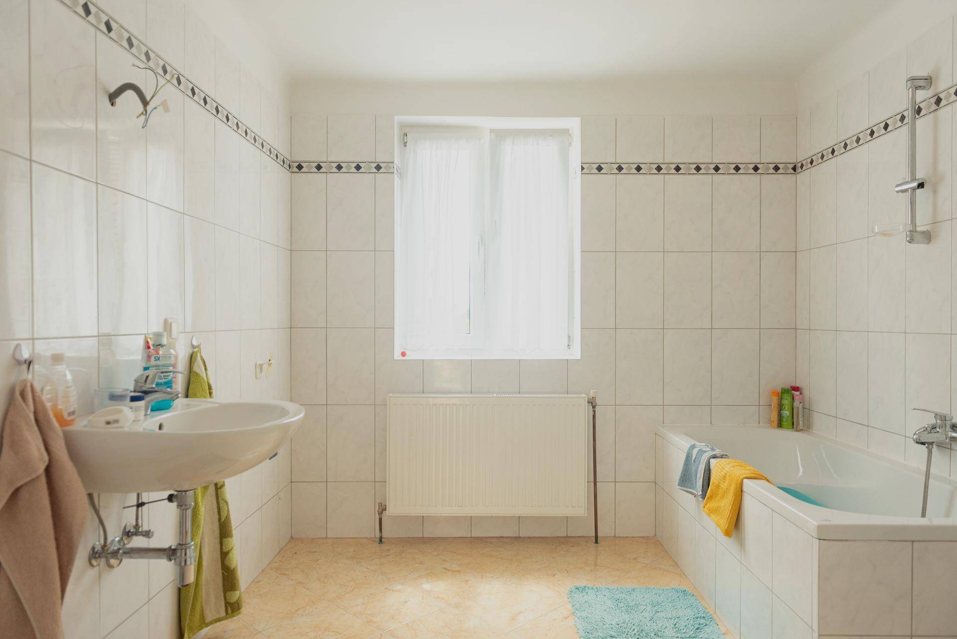 Helles Badezimmer mit weißen Fliesen, Badewanne, Waschbecken und Fenster.