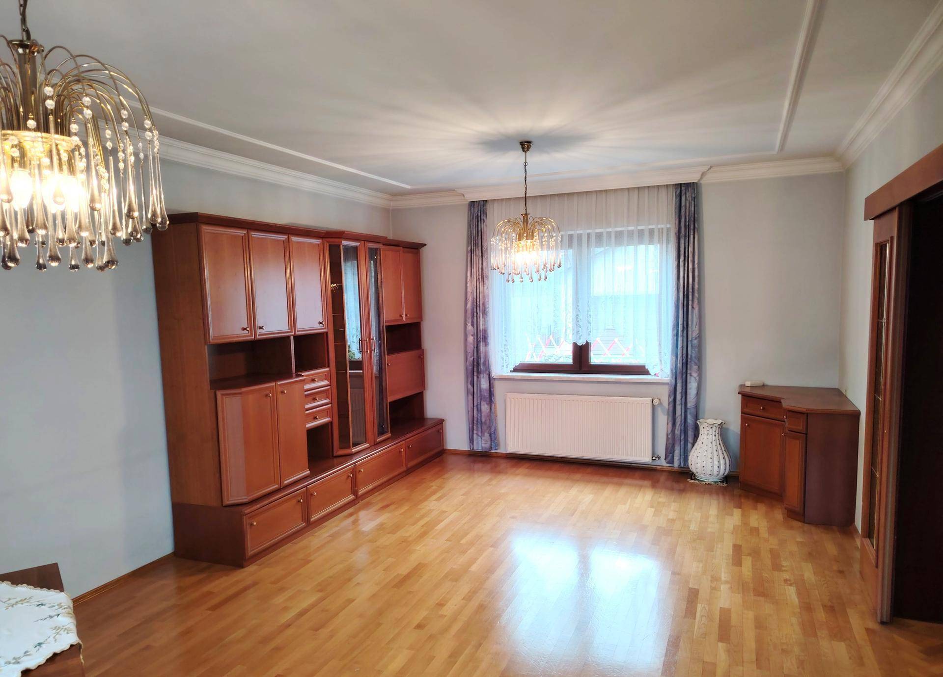 Geräumiges Wohnzimmer mit Parkettboden, großem Wandschrank und elegantem Kronleuchter.