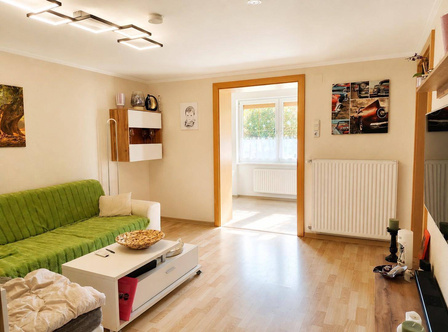 Helles Wohnzimmer mit modernem Sofa, Holzboden und Zugang zu einem weiteren Raum.