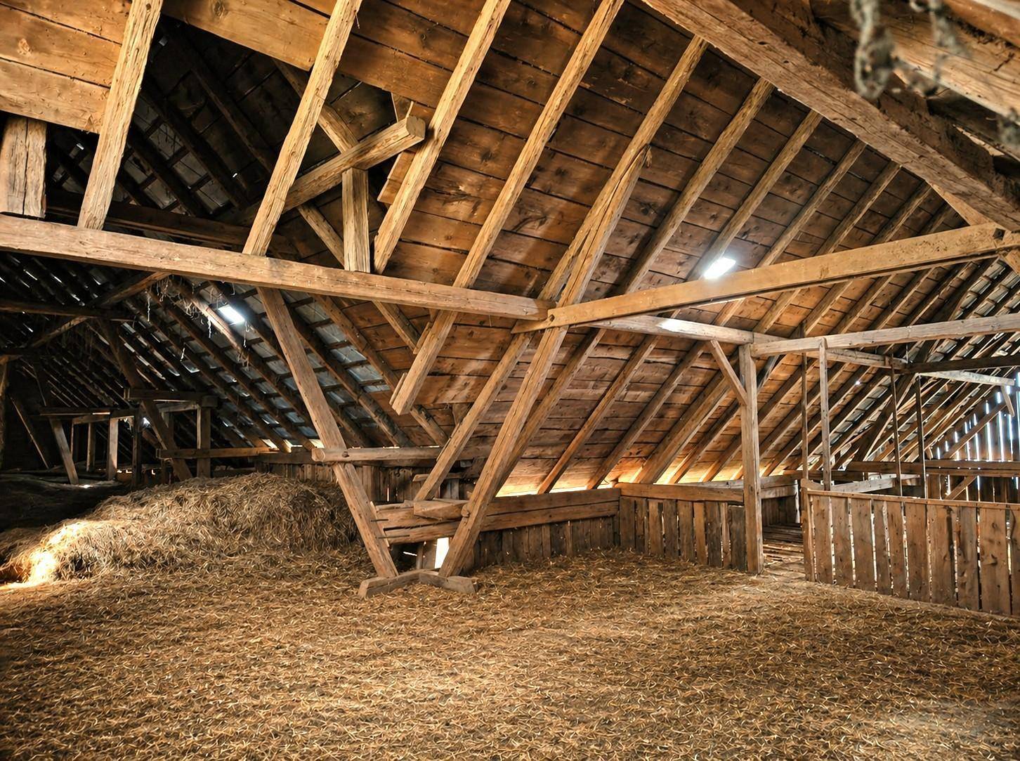 Geräumiger Scheuneninnenraum mit sichtbaren Holzbalken und Heuballen auf dem Boden.