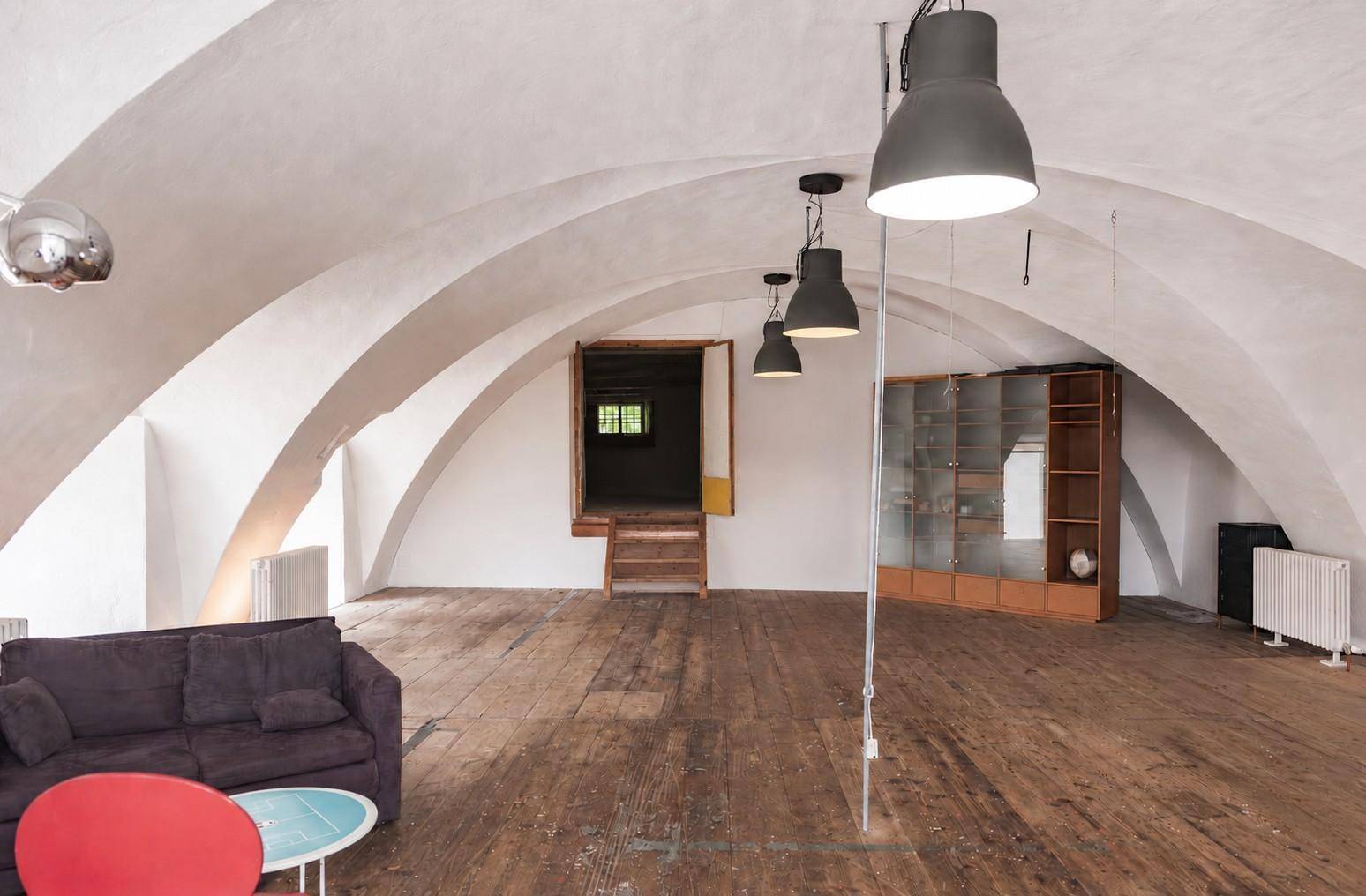 Geräumiger Wohnbereich mit eleganten Gewölbedecken, rustikalem Holzboden und einem Glasschrank.