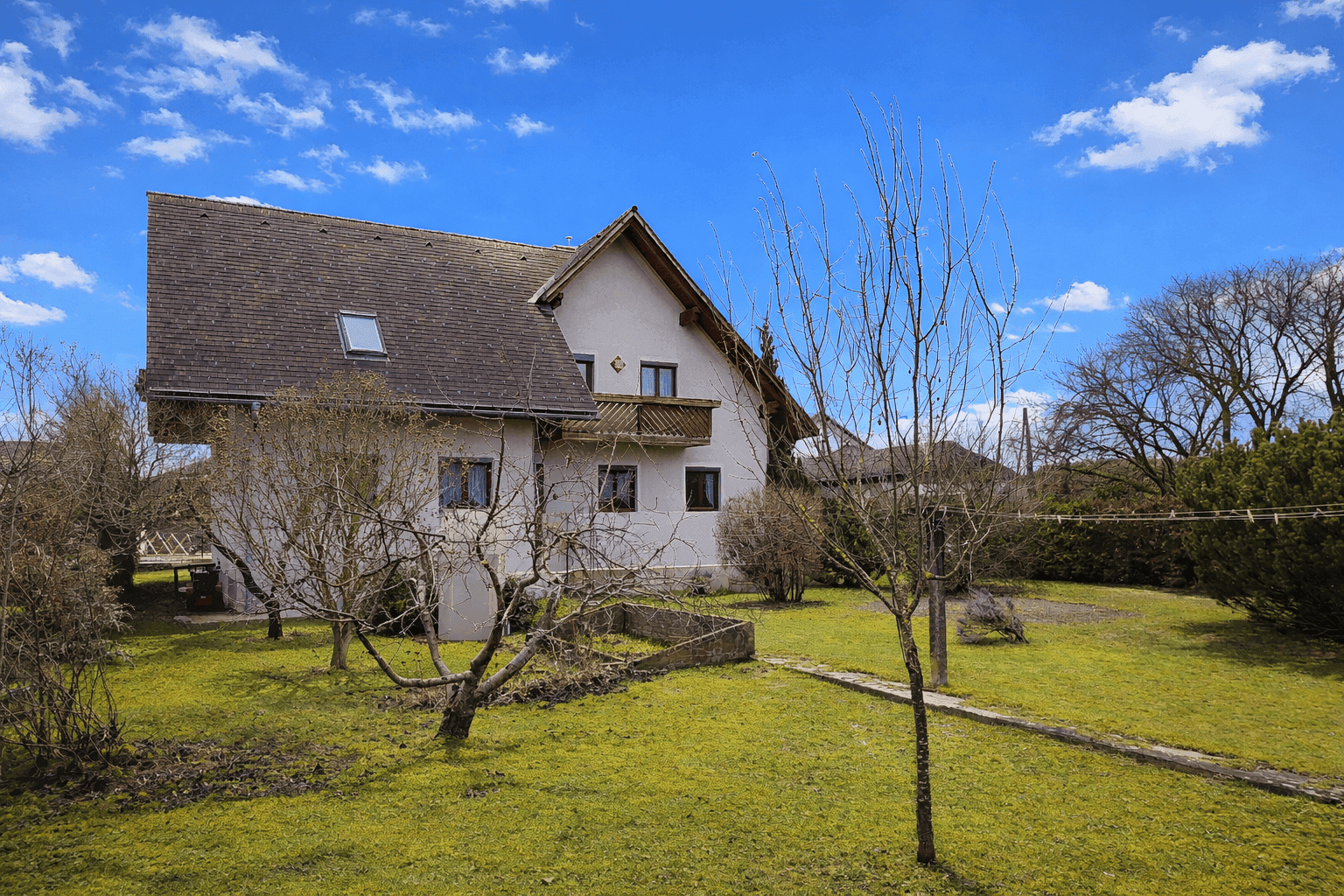 Einfamilienhaus mit großem Garten, Rasenfläche und Steinweg unter strahlend blauem Himmel.