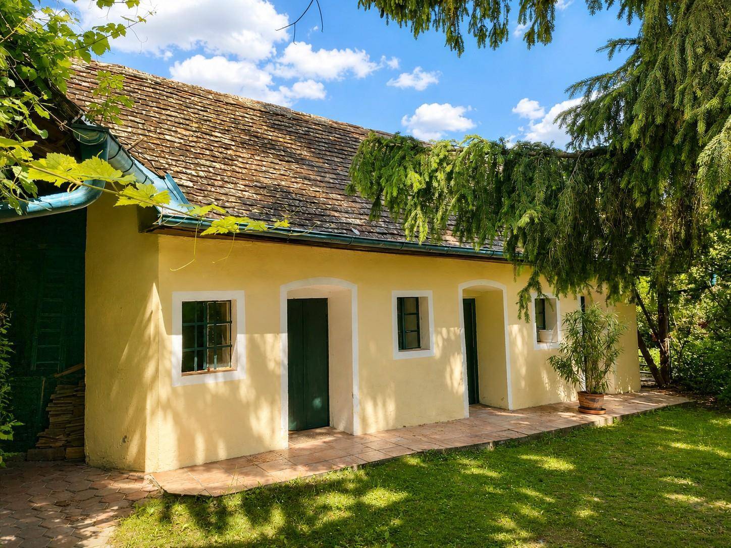 Traditionelles Haus mit gelber Fassade, grünen Türen und Fenstern, umgeben von einem gepflegten Garten.