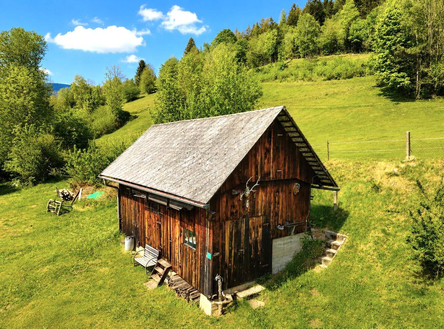 Rustikale Holzscheune mit Satteldach und Jagdtrophäen, eingebettet in grüne Natur.