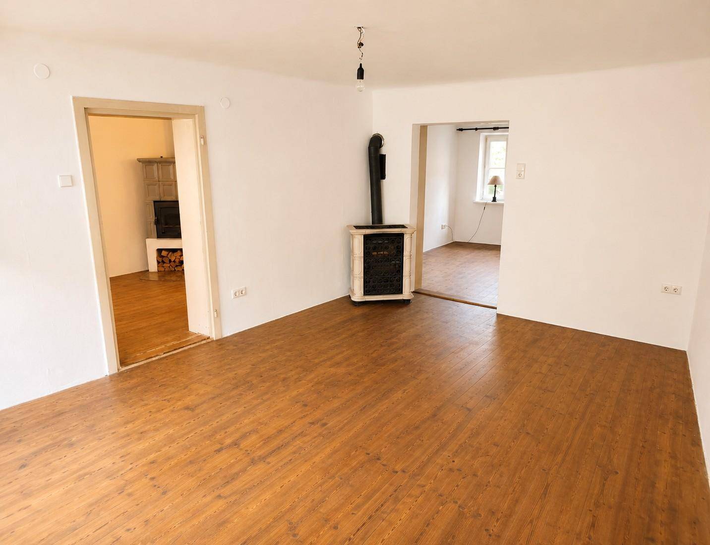 Geräumiges Wohnzimmer mit Holzdielenboden und einem traditionellen Kachelofen als Wärmequelle.