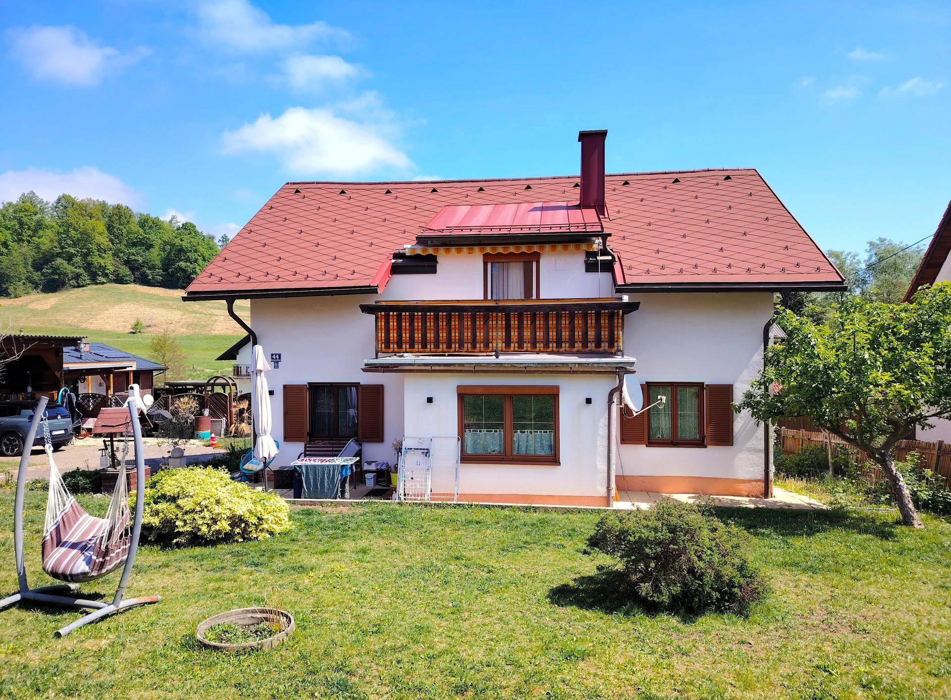 Rückansicht des Hauses mit Balkon, Terrasse und großem Garten unter blauem Himmel.