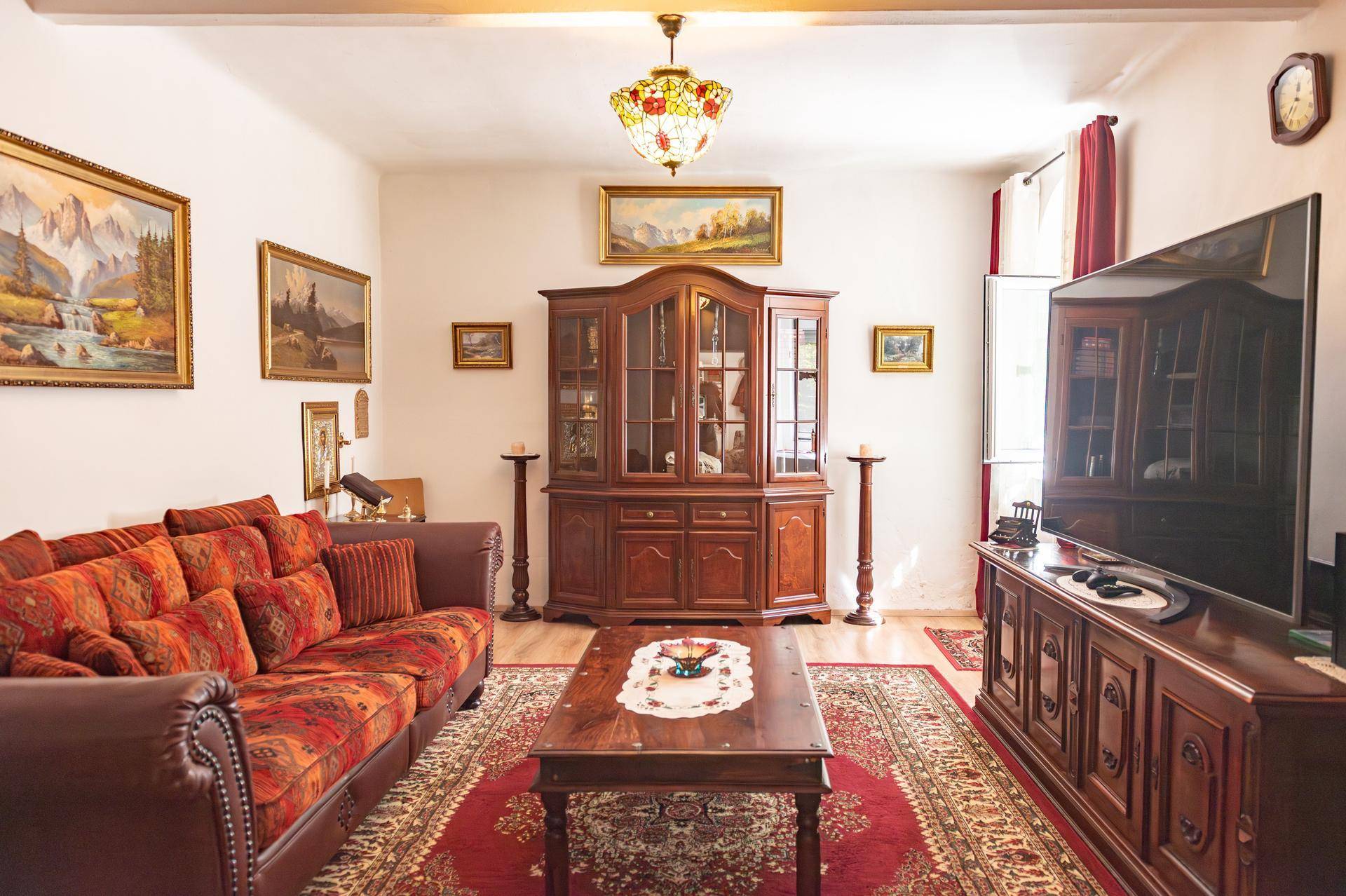 Traditionell eingerichtetes Wohnzimmer mit rotem Sofa, Holzmöbeln und Teppichboden.