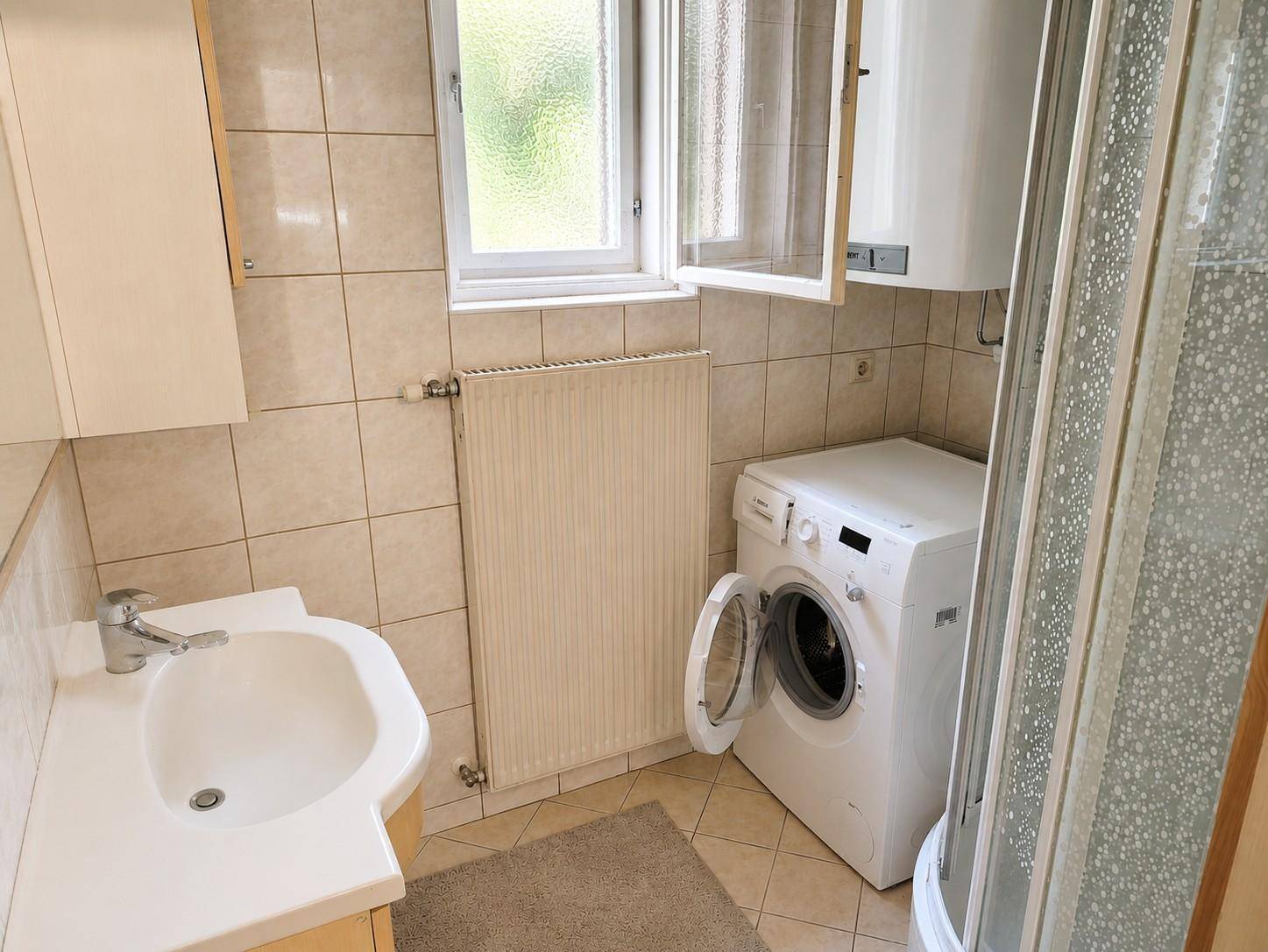 Funktionales Badezimmer mit Fliesenboden, Dusche, Waschbecken und Waschmaschine.