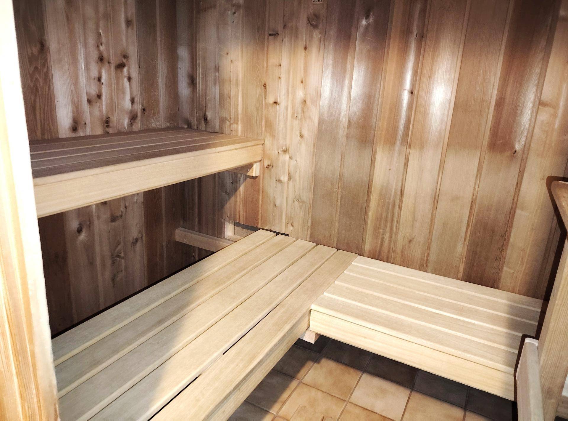 Holzverkleidete Sauna mit mehrstufigen Bänken und Fliesenboden, bereit zur Nutzung.