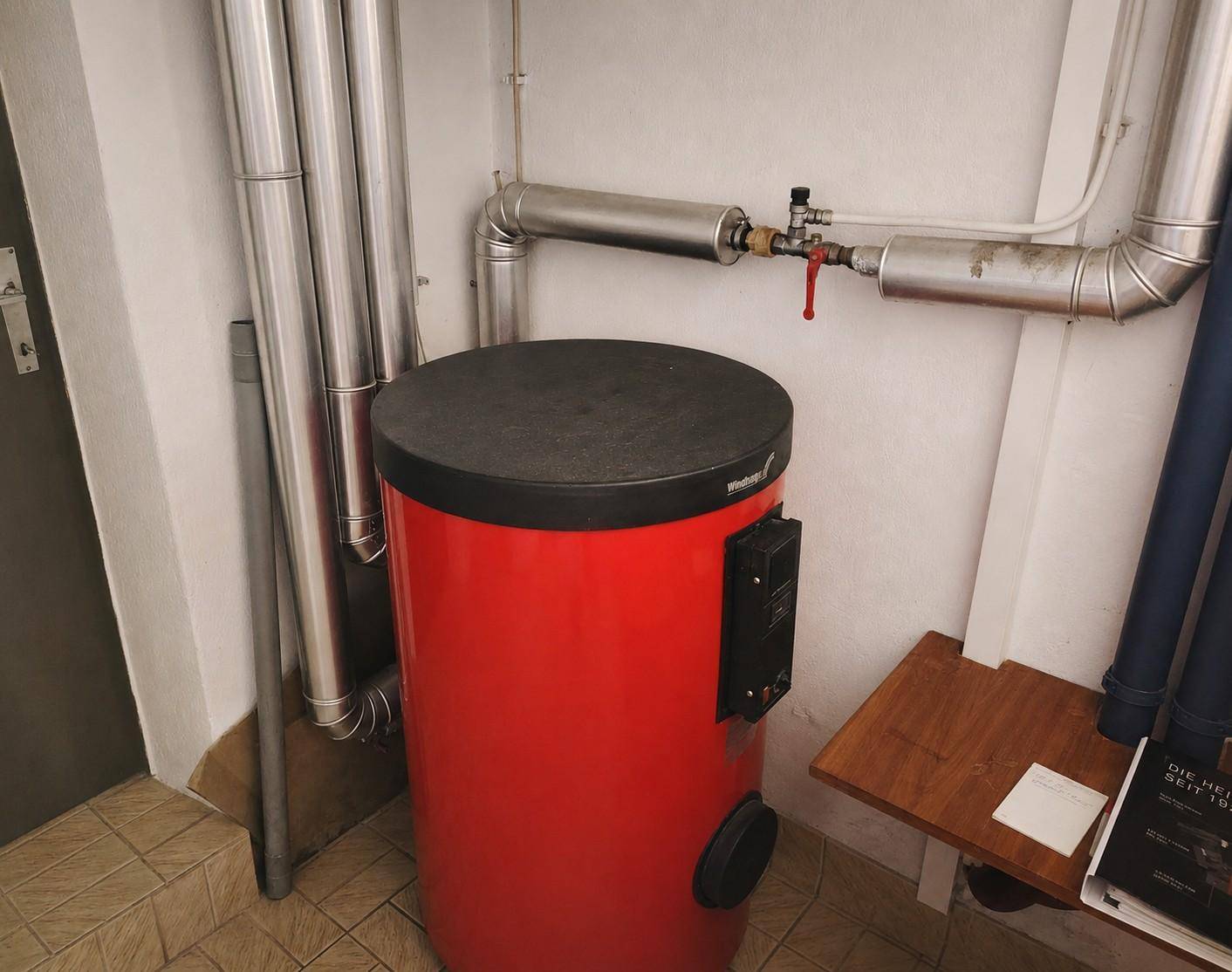 Heizungsraum mit großem Warmwasserspeicher und sichtbaren Rohrleitungen.