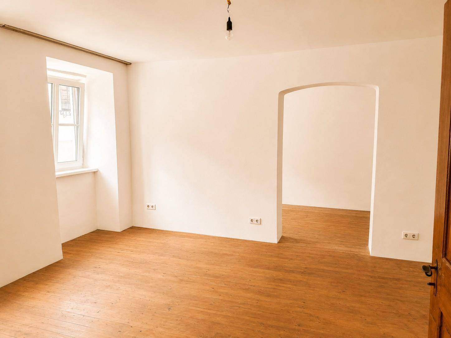 Helles Zimmer mit Holzboden und weiß gestrichenen Wänden, bereit für die individuelle Gestaltung.