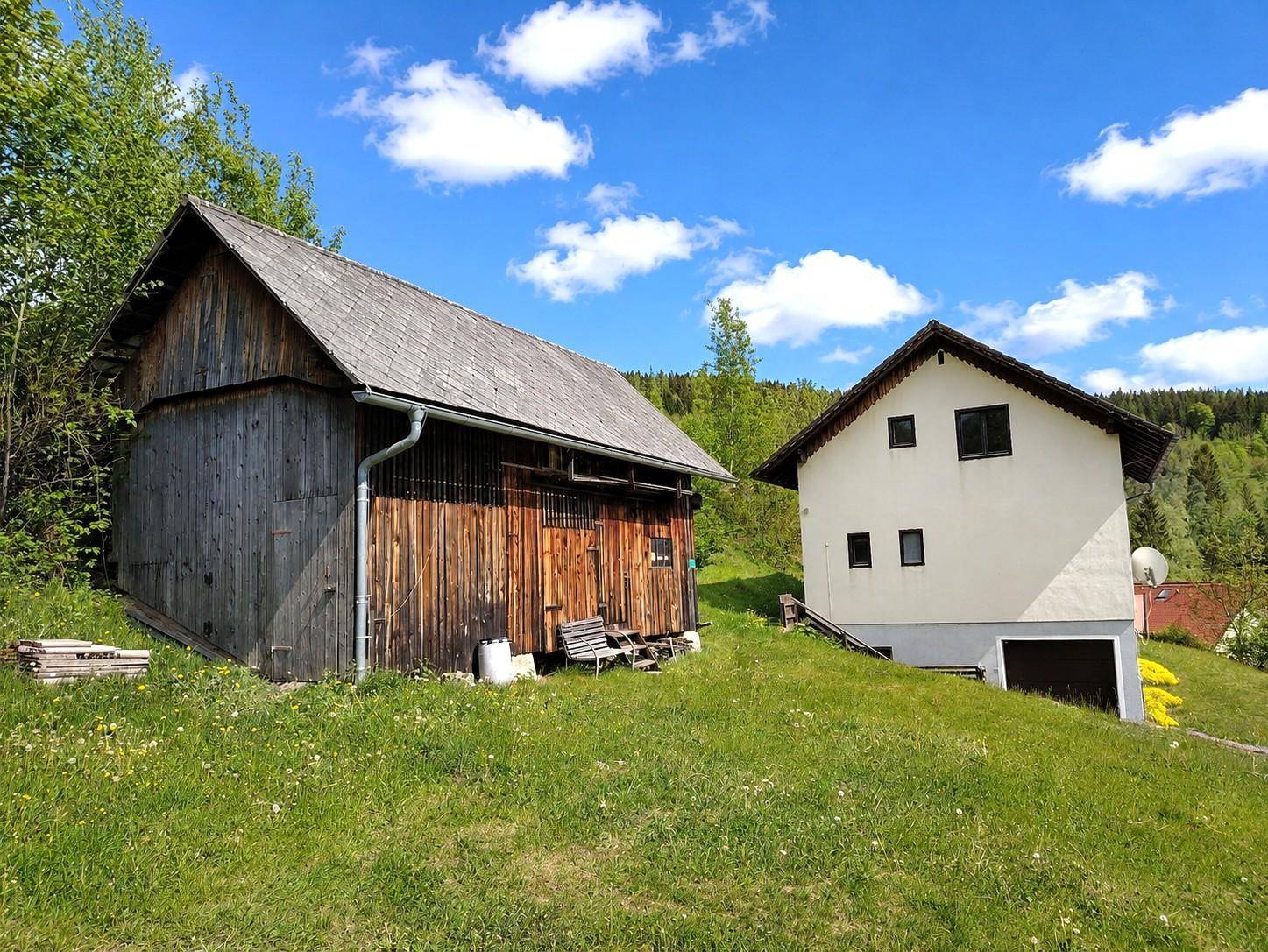 Ländliches Anwesen mit Haupthaus und rustikaler Holzscheune auf einem grünen Hügel.
