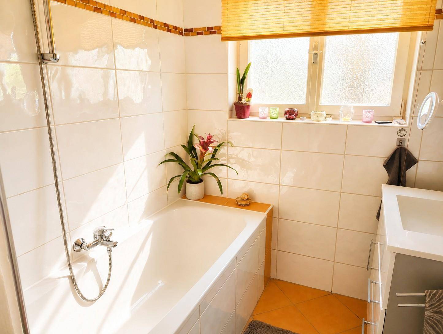 Helles Badezimmer mit Badewanne, Dusche, Fenster und weißen Fliesen.