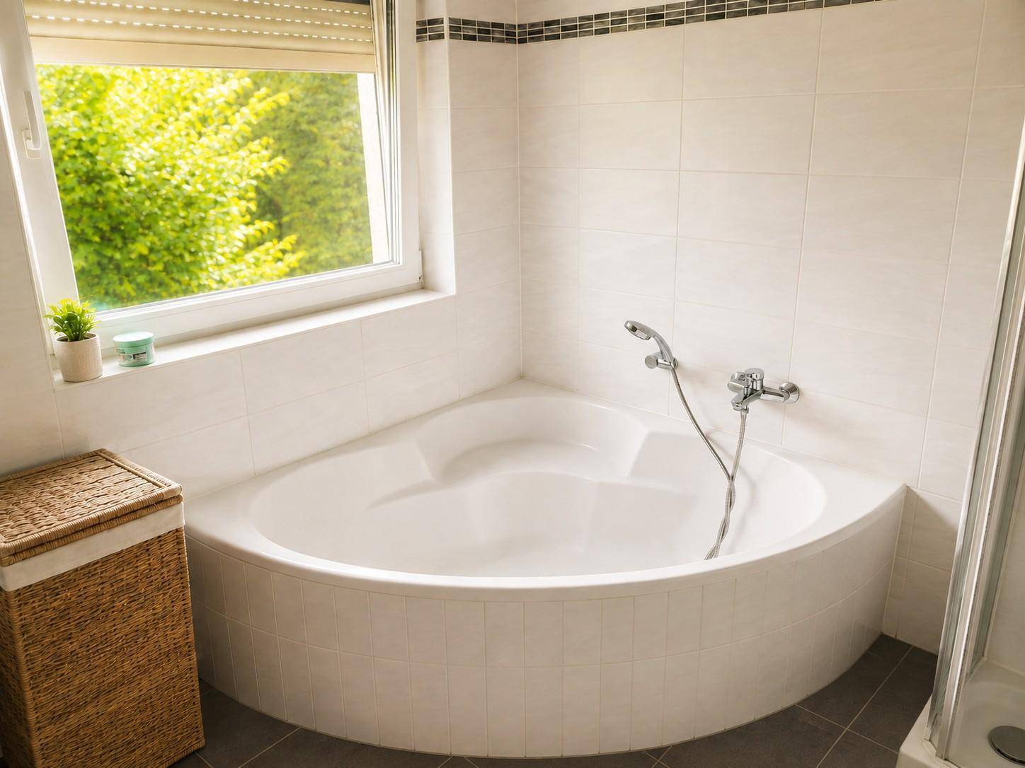 Badezimmer mit Eckbadewanne, Fliesenboden und Fenster mit Blick ins Grüne.
