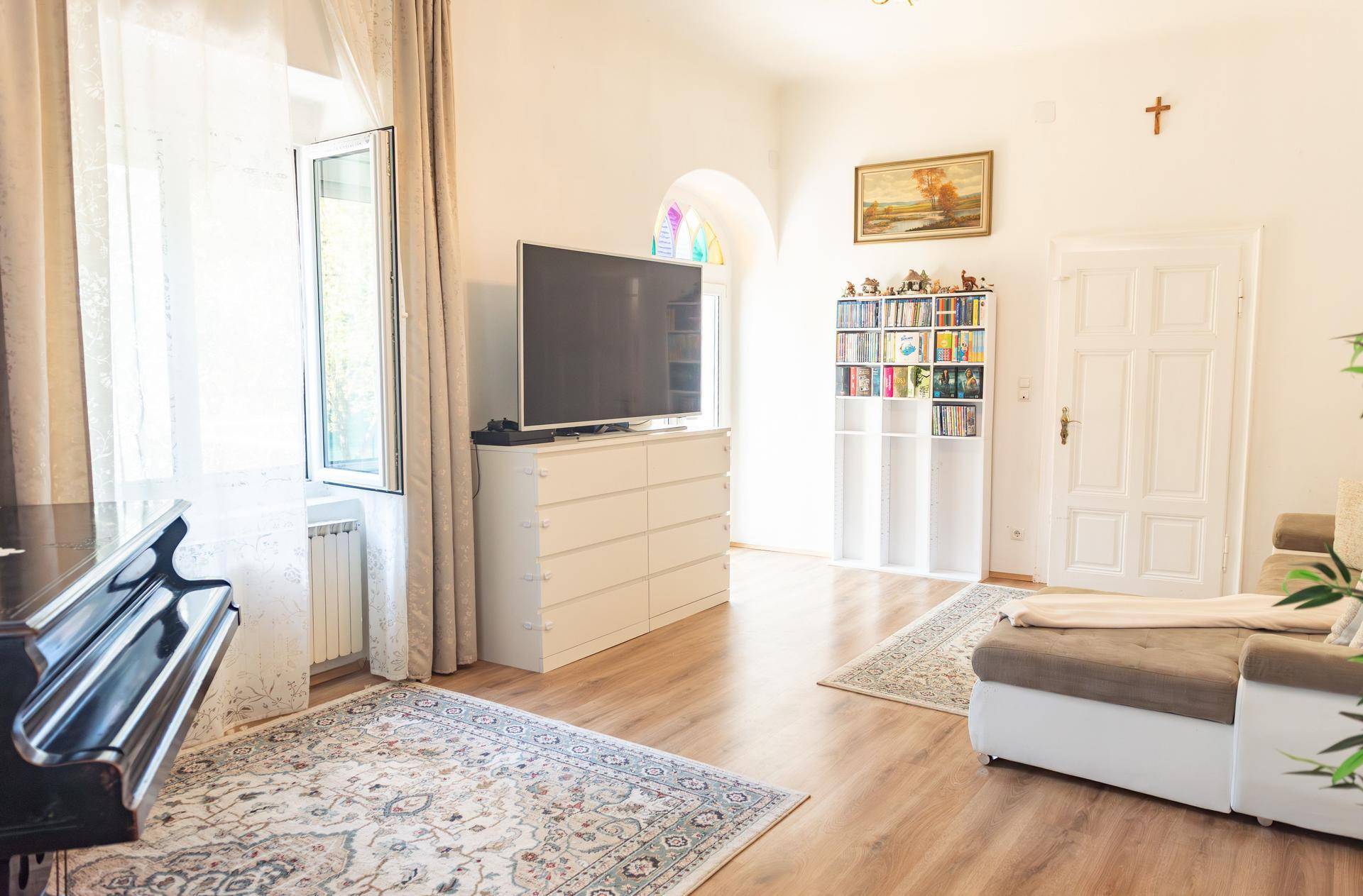 Helles Wohnzimmer mit Holzboden, großem Fernseher und Bücherregal, mit Blick ins Grüne.