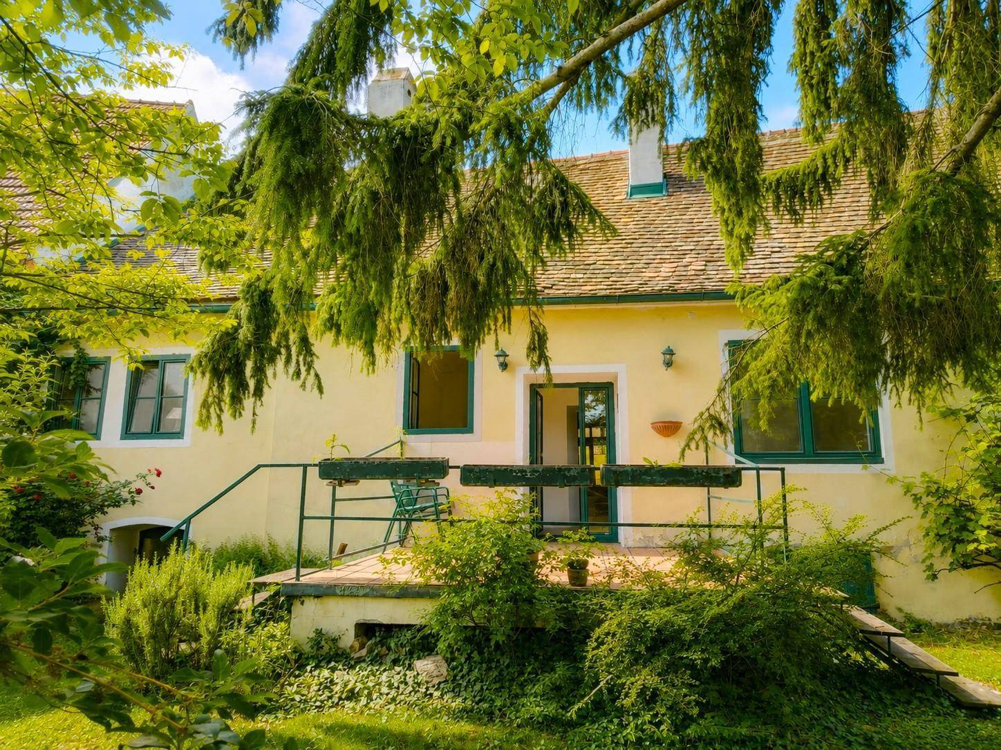 Kleine Terrasse mit grünem Geländer und Sitzgelegenheit, umgeben von üppiger Vegetation.