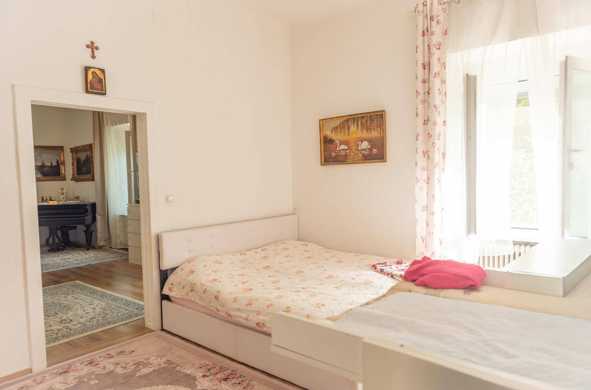 Helles Schlafzimmer mit Bett und Fenster, das einen Blick in einen anderen Raum bietet.