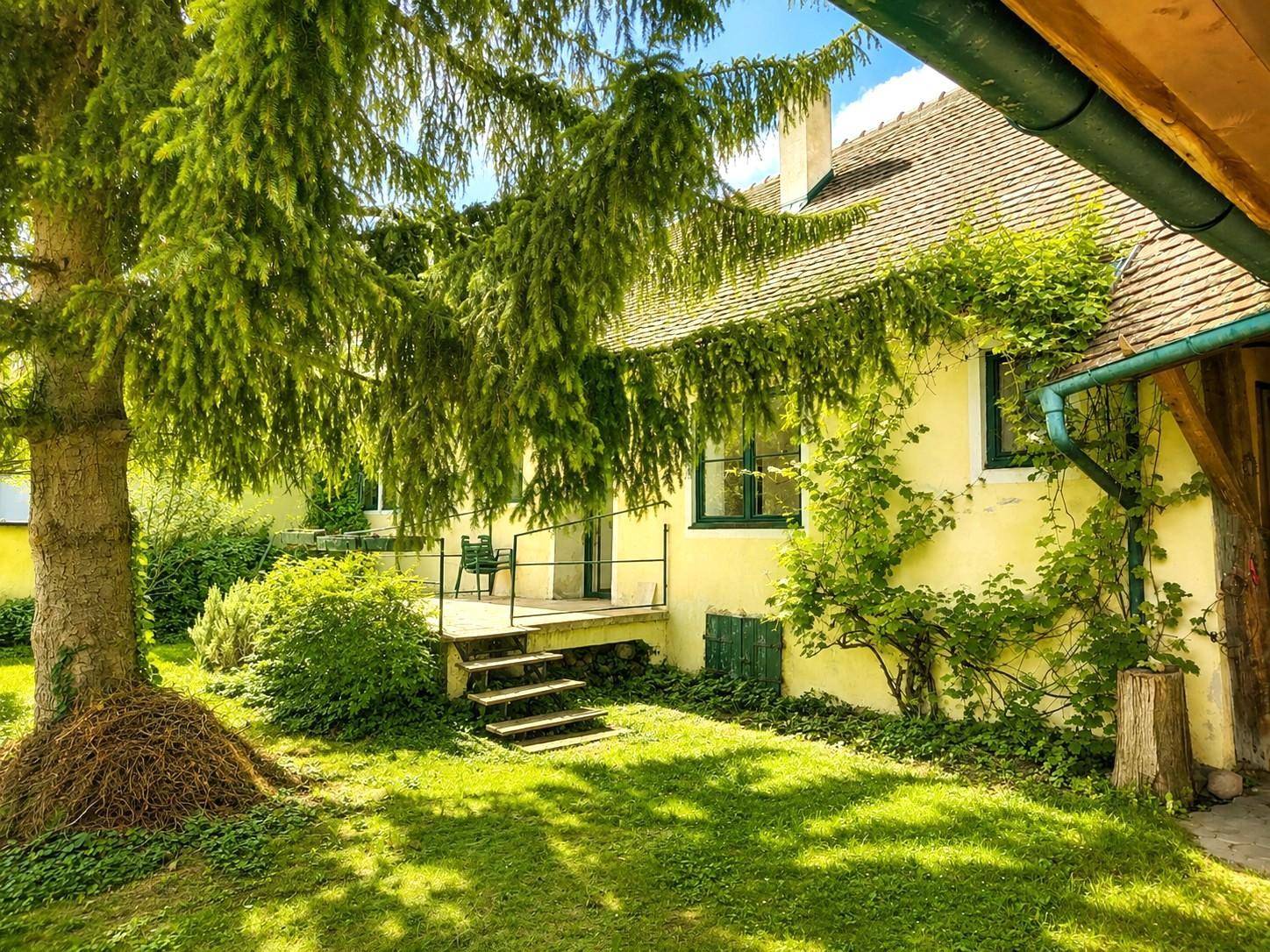 Idyllischer Gartenbereich mit altem Baumbestand und Blick auf die traditionelle Hausfassade mit Terrasse.