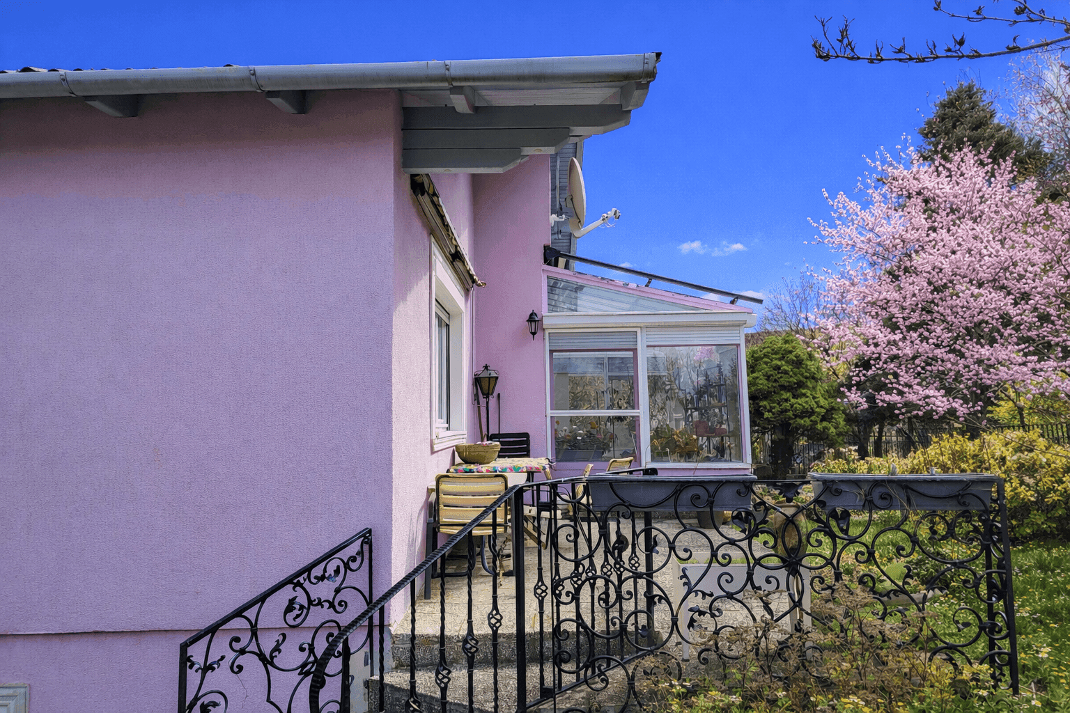 Kleine Terrasse am rosa Haus mit schmiedeeisernem Geländer und Blick in den Garten.