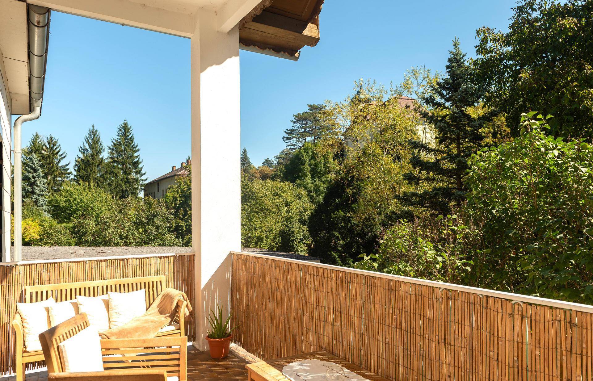 Sonniger Balkon mit bequemen Holzmöbeln und einem schönen Blick ins Grüne.