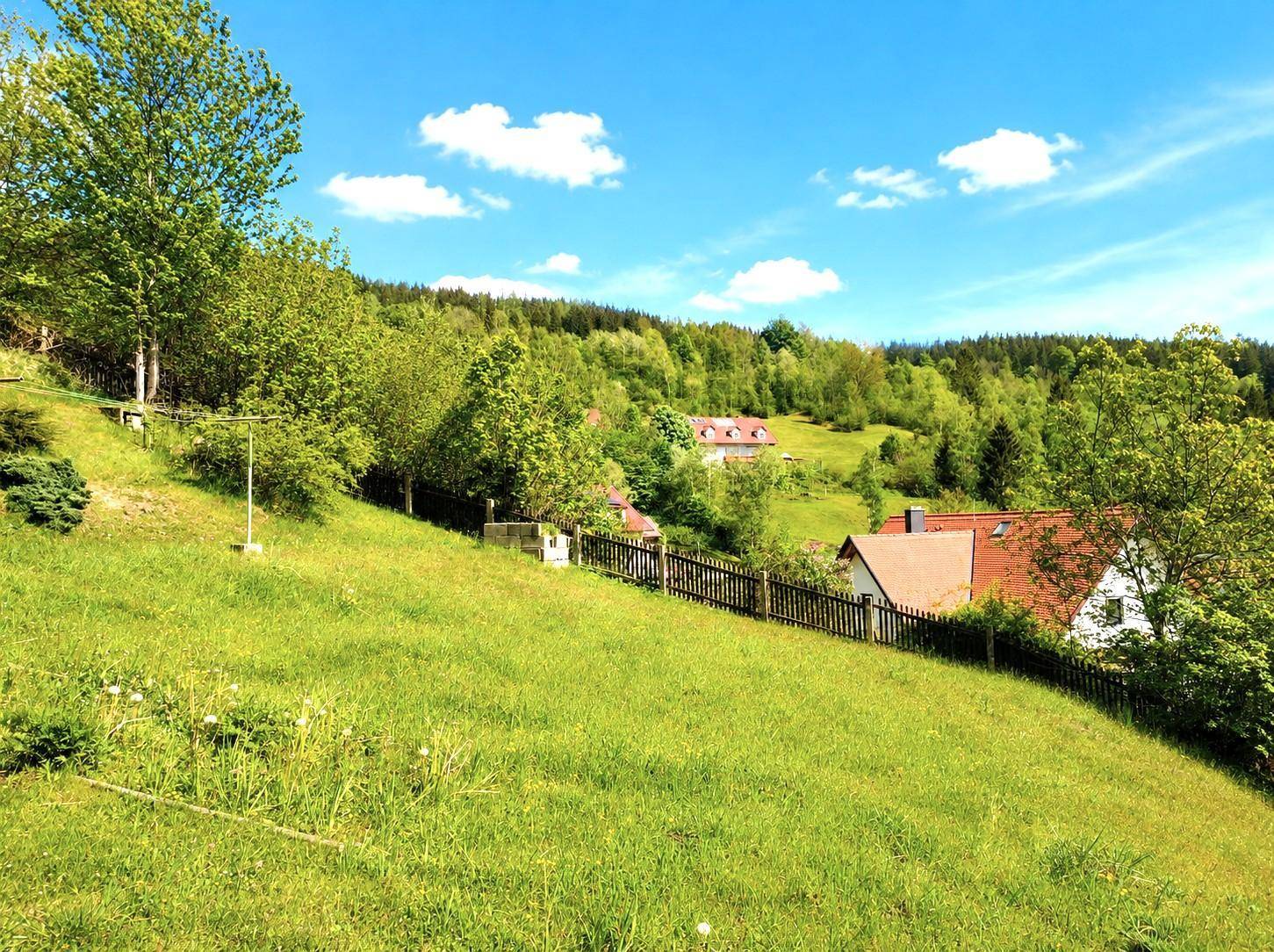 Weitläufige grüne Landschaft mit bewaldeten Hügeln und vereinzelten Häusern in der Ferne.