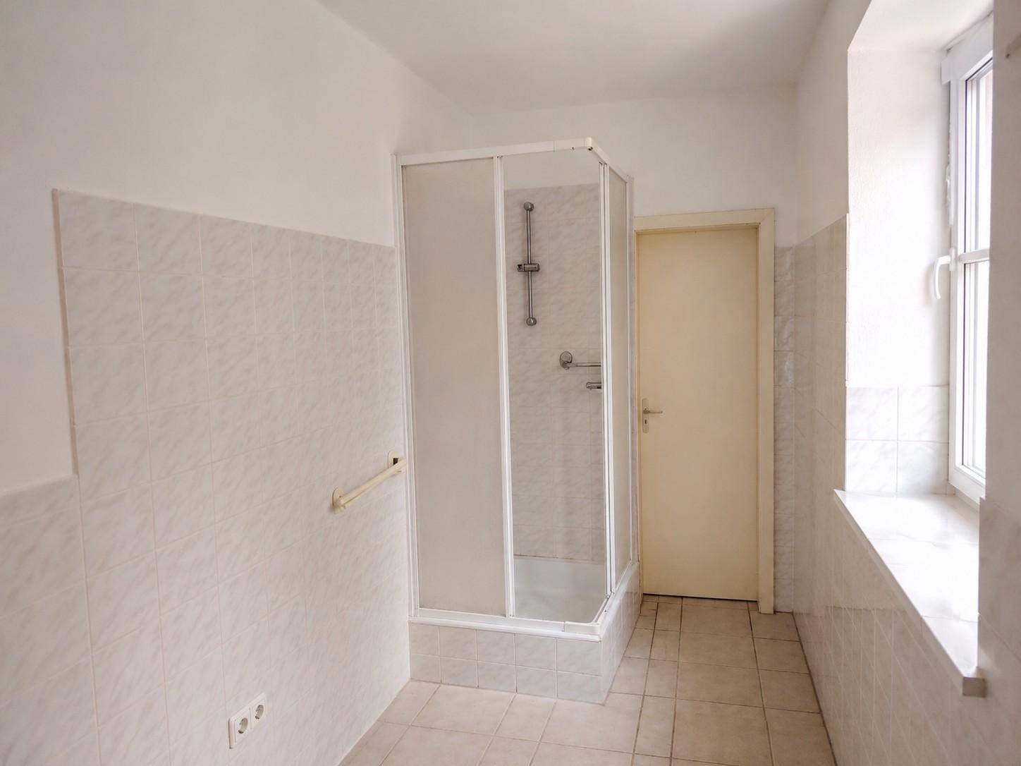 Helles Badezimmer mit Duschkabine, weißen Fliesen und einem Fenster für Tageslicht.