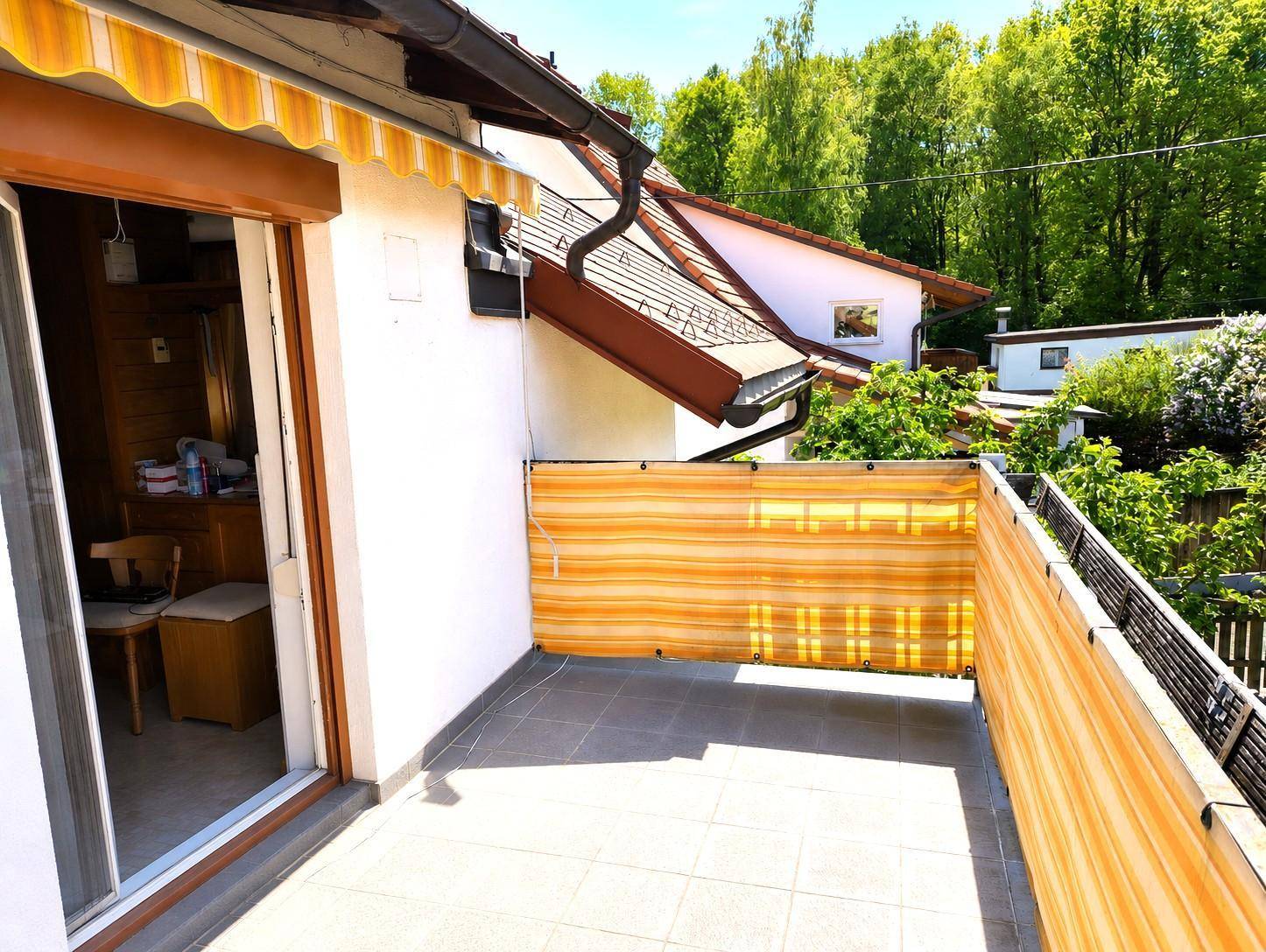 Kleiner Balkon mit Fliesenboden, Sichtschutz und Blick auf die umliegende Natur.