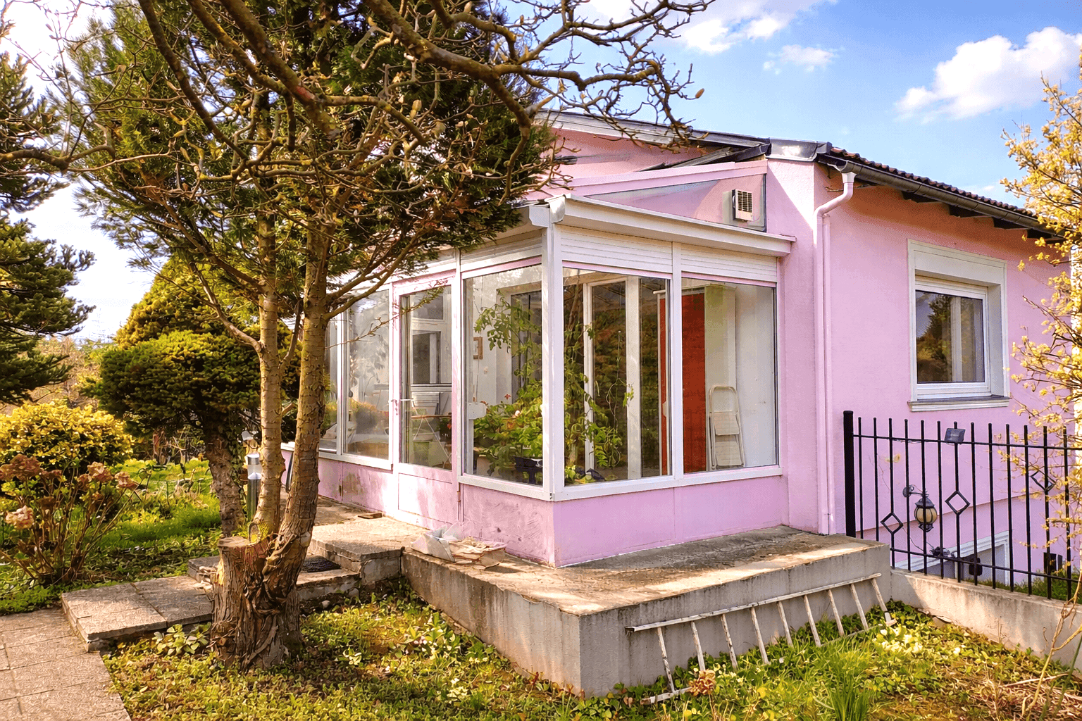 Seitlicher Blick auf das rosa Haus mit Wintergarten und einem gepflegten Gartenbereich.