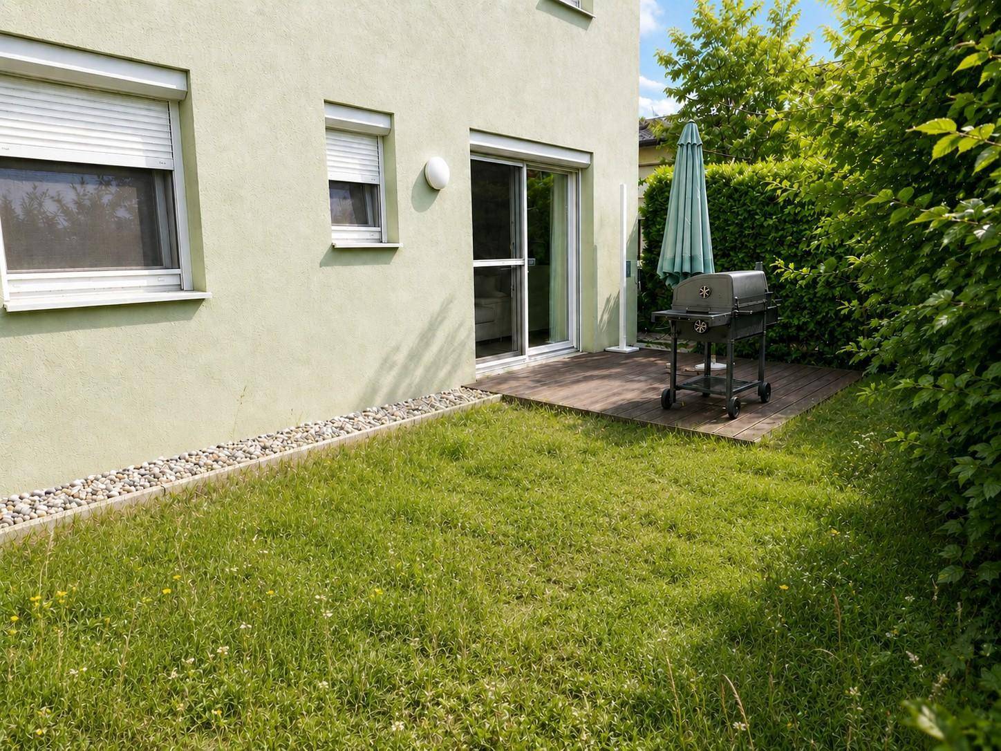 Kleiner Gartenbereich mit Rasenfläche, Grill und Zugang zur Terrasse.