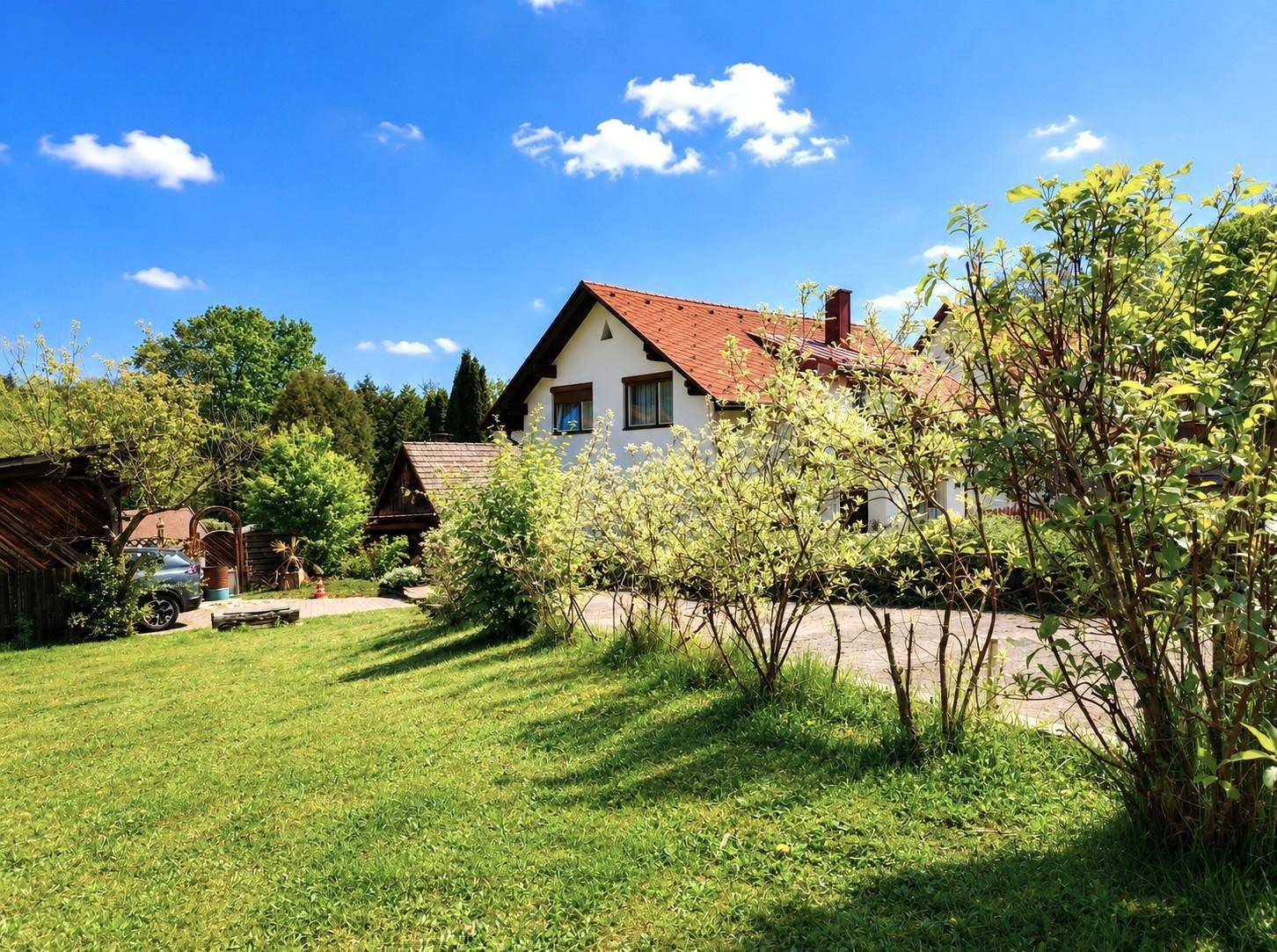 Hausansicht von der Seite mit großem Garten, gepflegtem Rasen und üppiger Bepflanzung.