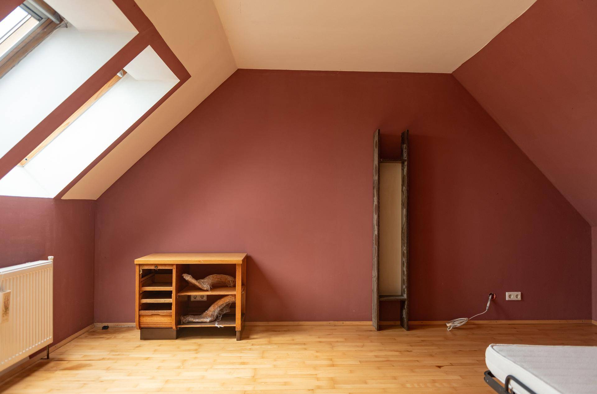 Geräumiges Zimmer im Dachgeschoss mit roter Wand, Holzboden und Dachfenstern.