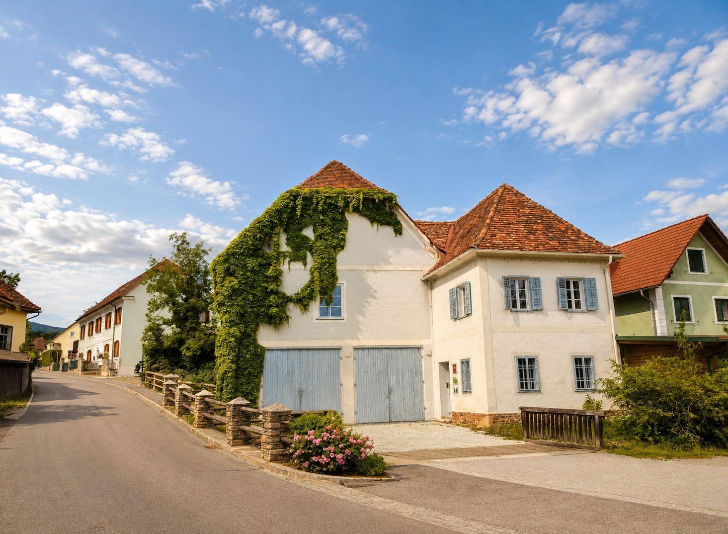 Vorderansicht eines historischen Gebäudes mit blauen Garagentoren, Fensterläden und einem kleinen Vorgarten.