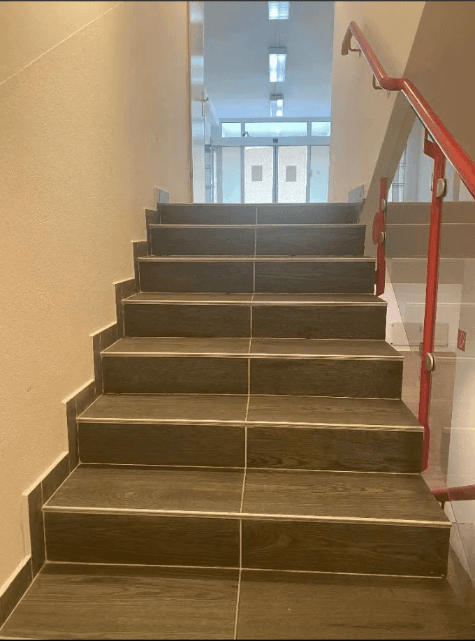 Detailansicht der Treppe mit dunklen Fliesenstufen und einem roten Handlauf, der nach oben führt.