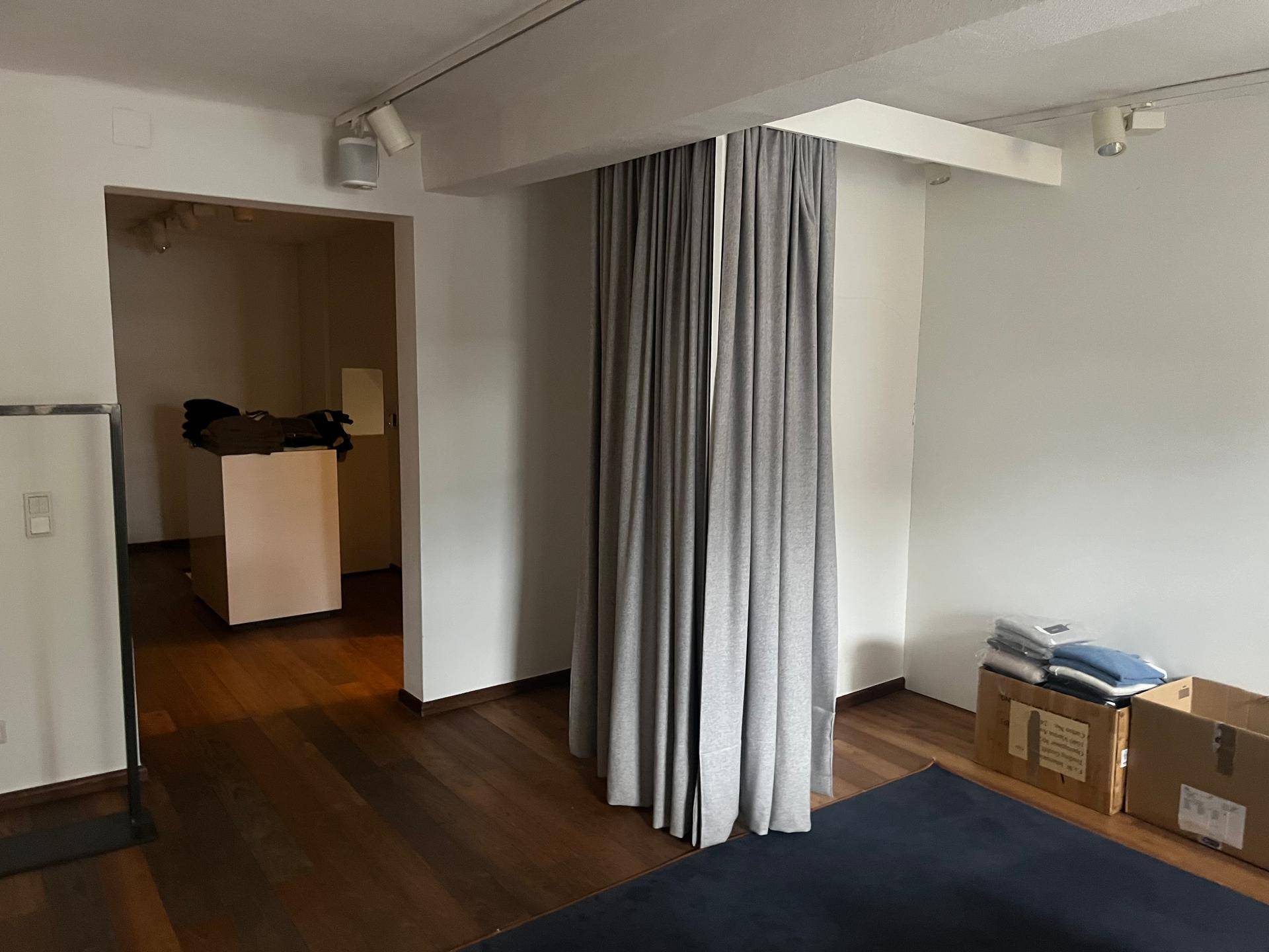 Innenraum mit Holzboden, Vorhängen als Raumteiler und einem Durchgang zu einem weiteren Bereich.