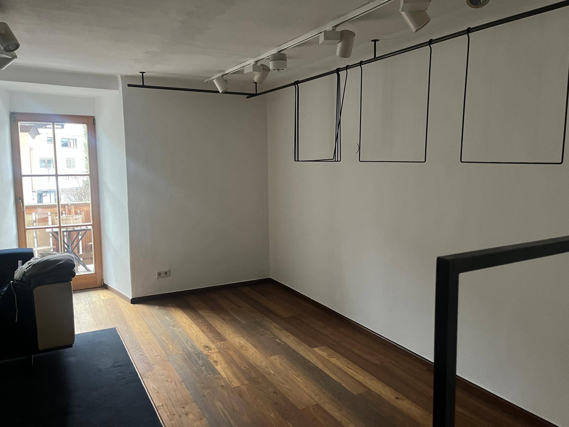 Heller Raum im Obergeschoss mit Holzboden, weißen Wänden und einer Tür, die zu einem kleinen Balkon führt.