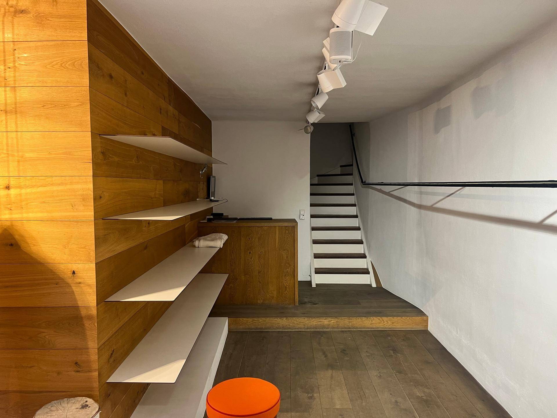 Innenansicht eines Ladenlokals mit Holzvertäfelung, Regalen und einer Treppe zum oberen Bereich.