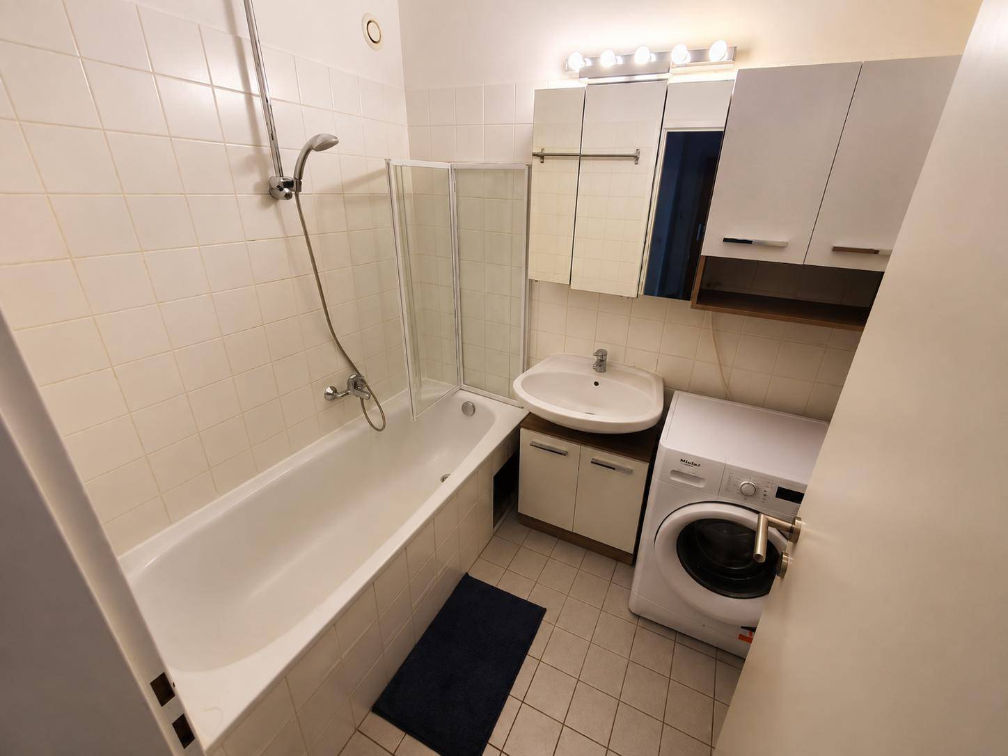 Funktionales Badezimmer mit Badewanne, Waschbecken, Fliesen und Waschmaschine.