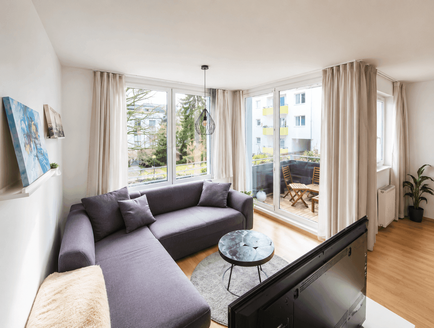 Gemütliches Wohnzimmer mit großem Sofa, Holzboden und Zugang zu einem Balkon.