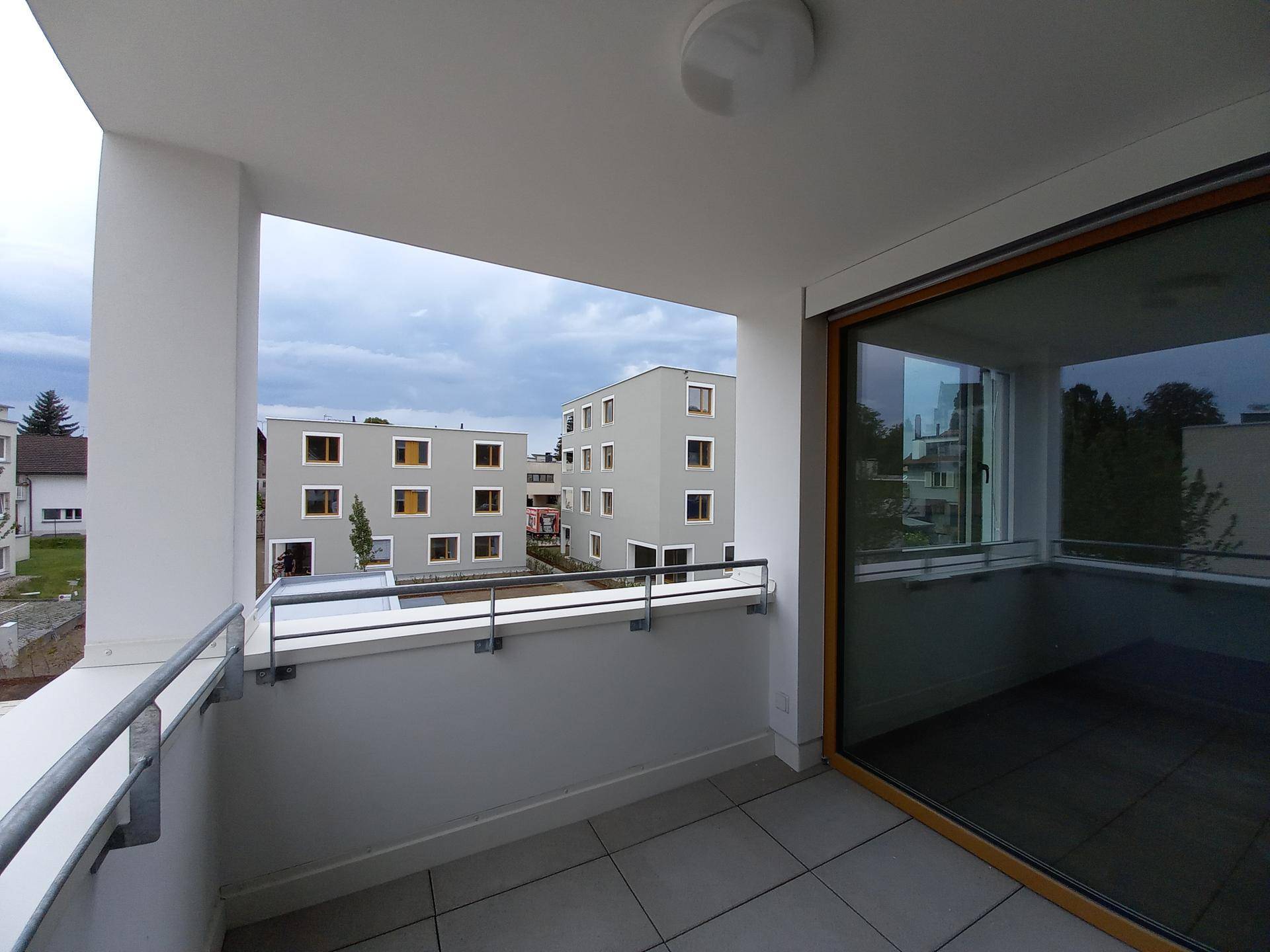 Heller Balkon mit Fliesenboden und Metallgeländer, bietet Blick auf die umliegenden modernen Wohngebäude.