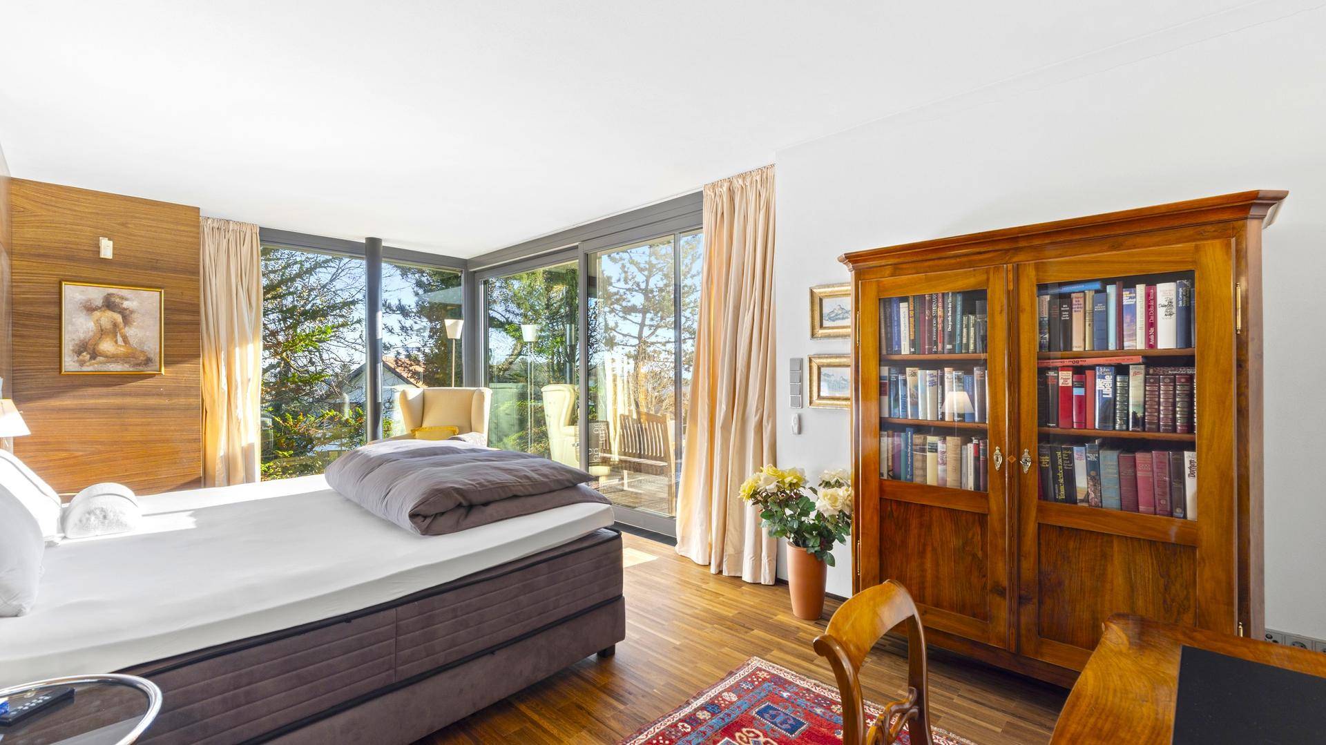 Helles Schlafzimmer mit großzügigen Fenstern, Holzboden und Zugang zur Terrasse.