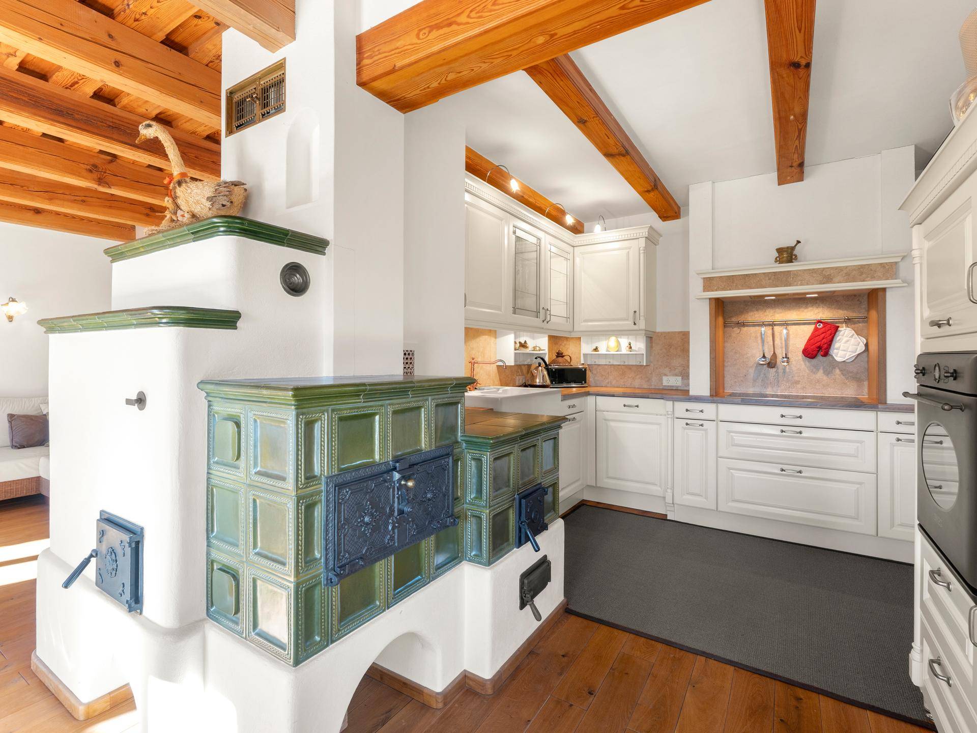 Traditionelle Küche mit weißer Einbauküche, Holzbalken und einem charmanten Kachelofen.