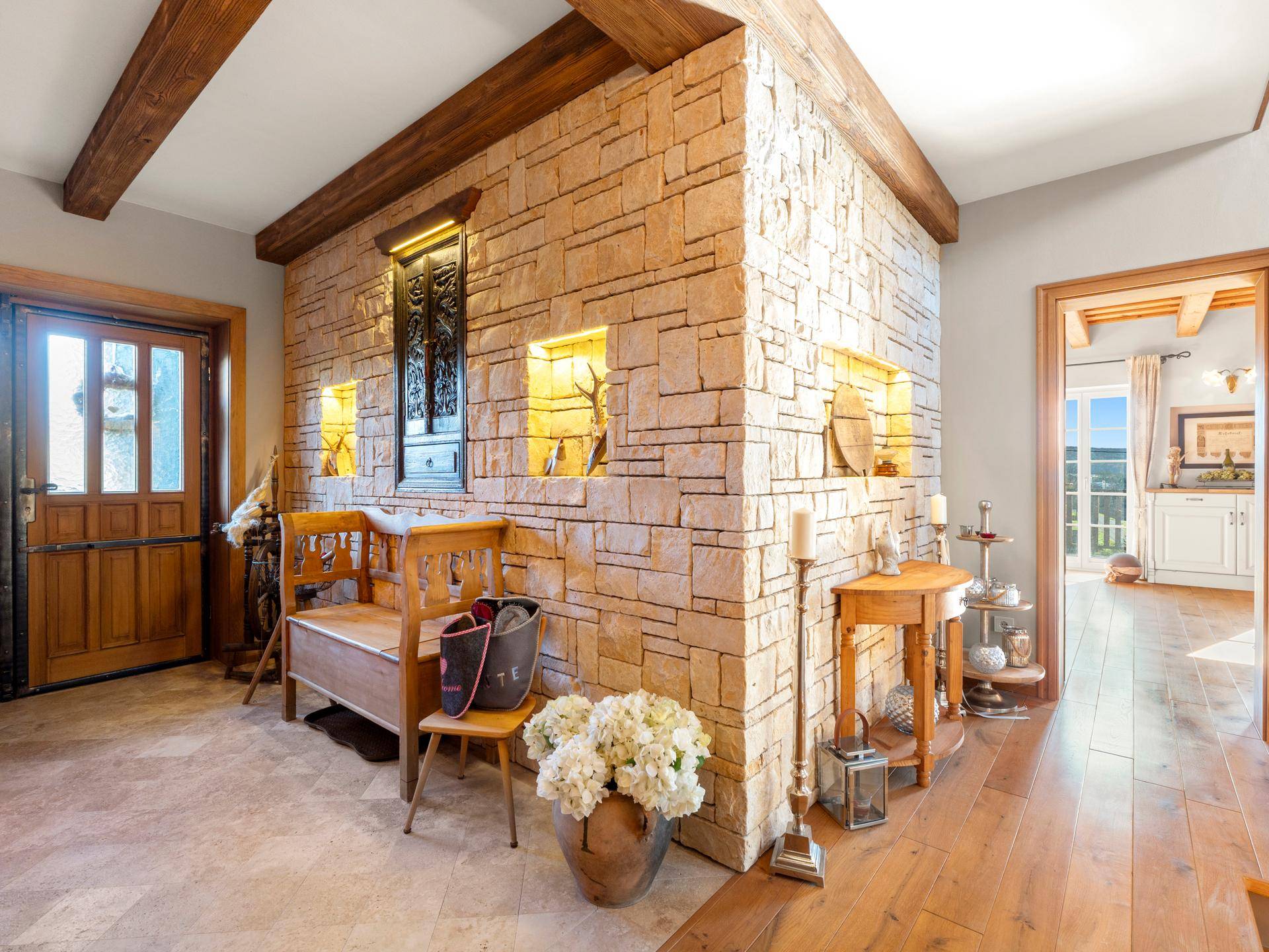 Einladender Eingangsbereich mit Steinwand, Holzbalken und rustikalen Möbeln.