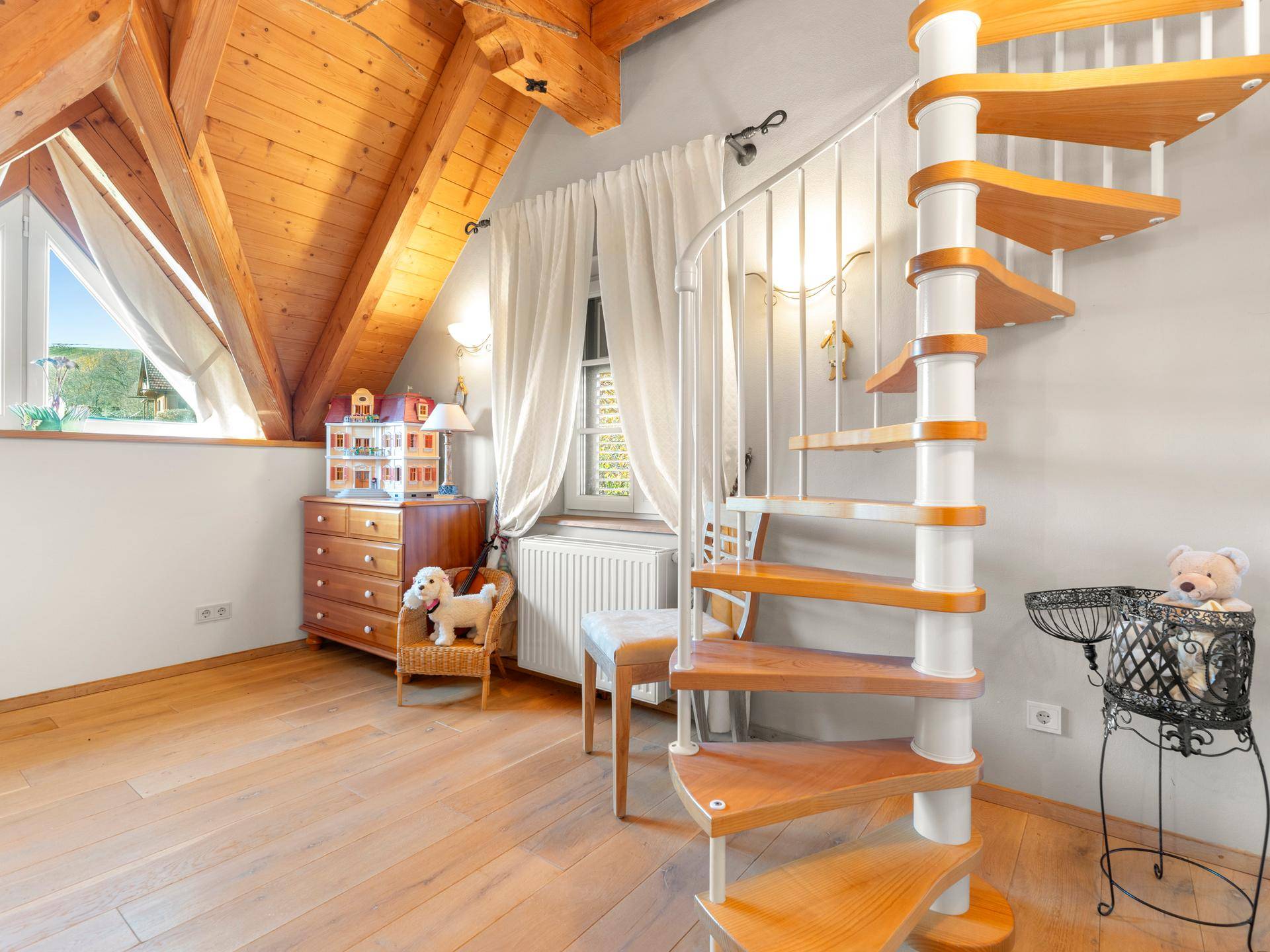 Helles Kinderzimmer im Dachgeschoss mit Holzbalken, Wendeltreppe und schrägen Wänden.