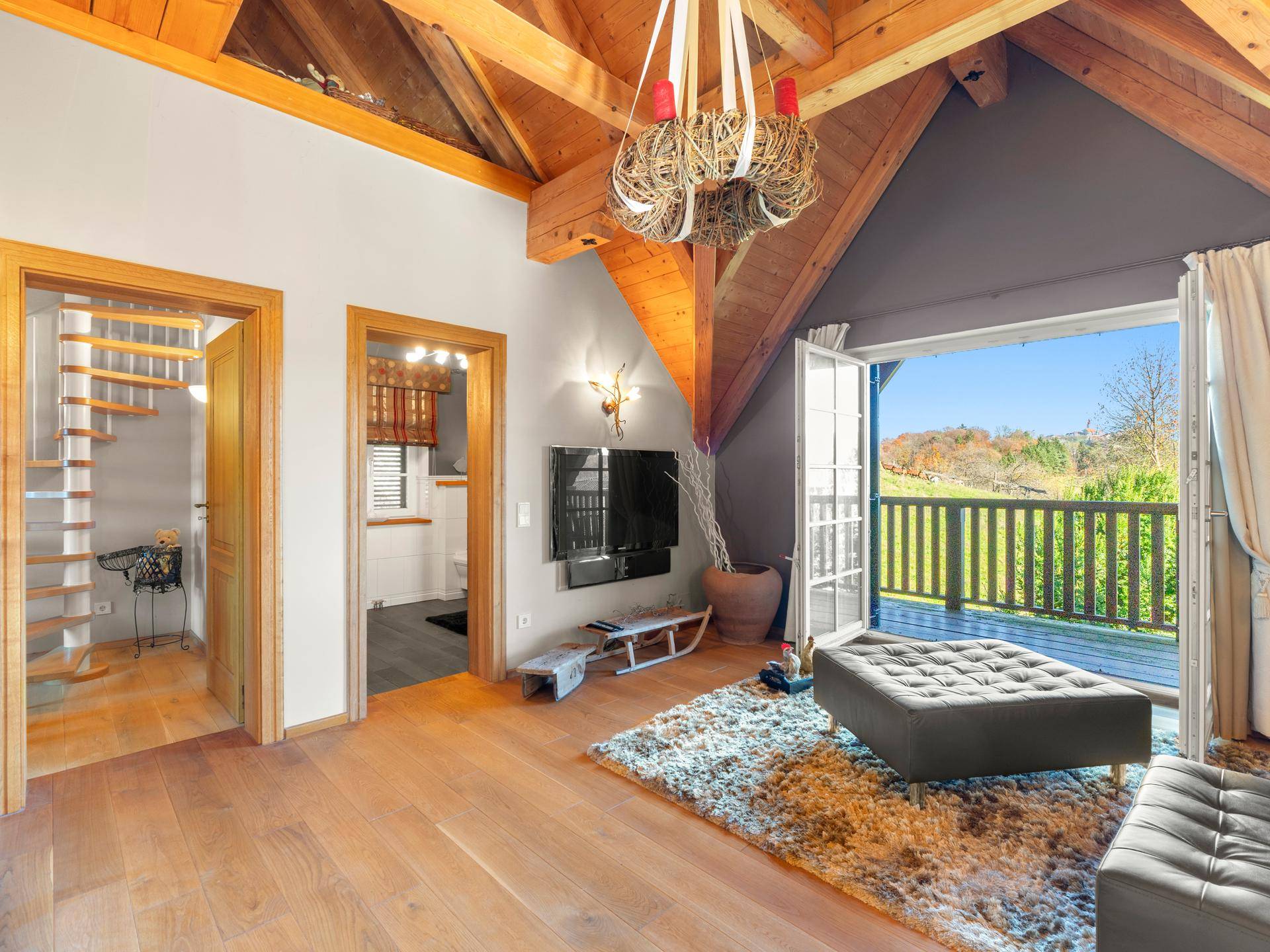 Gemütlicher Wohnbereich im Dachgeschoss mit Holzbalken, Parkettboden und Zugang zum Balkon.